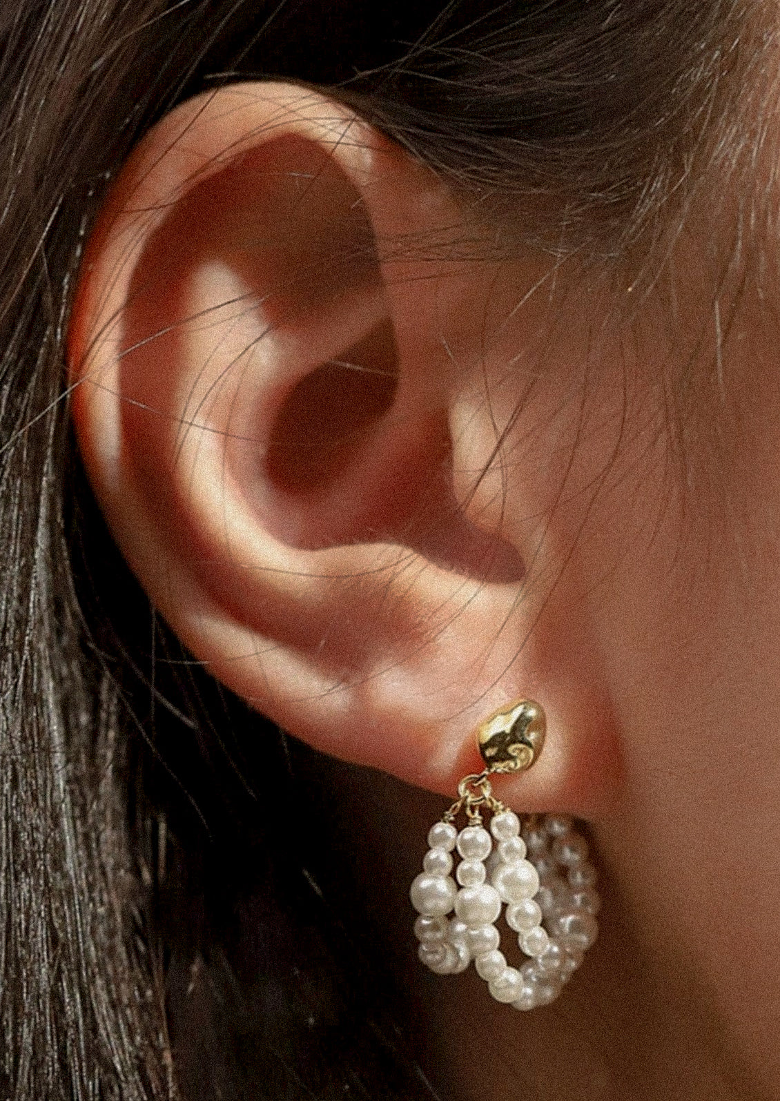 A woman wearing an earring that has three strands of faux pearls.