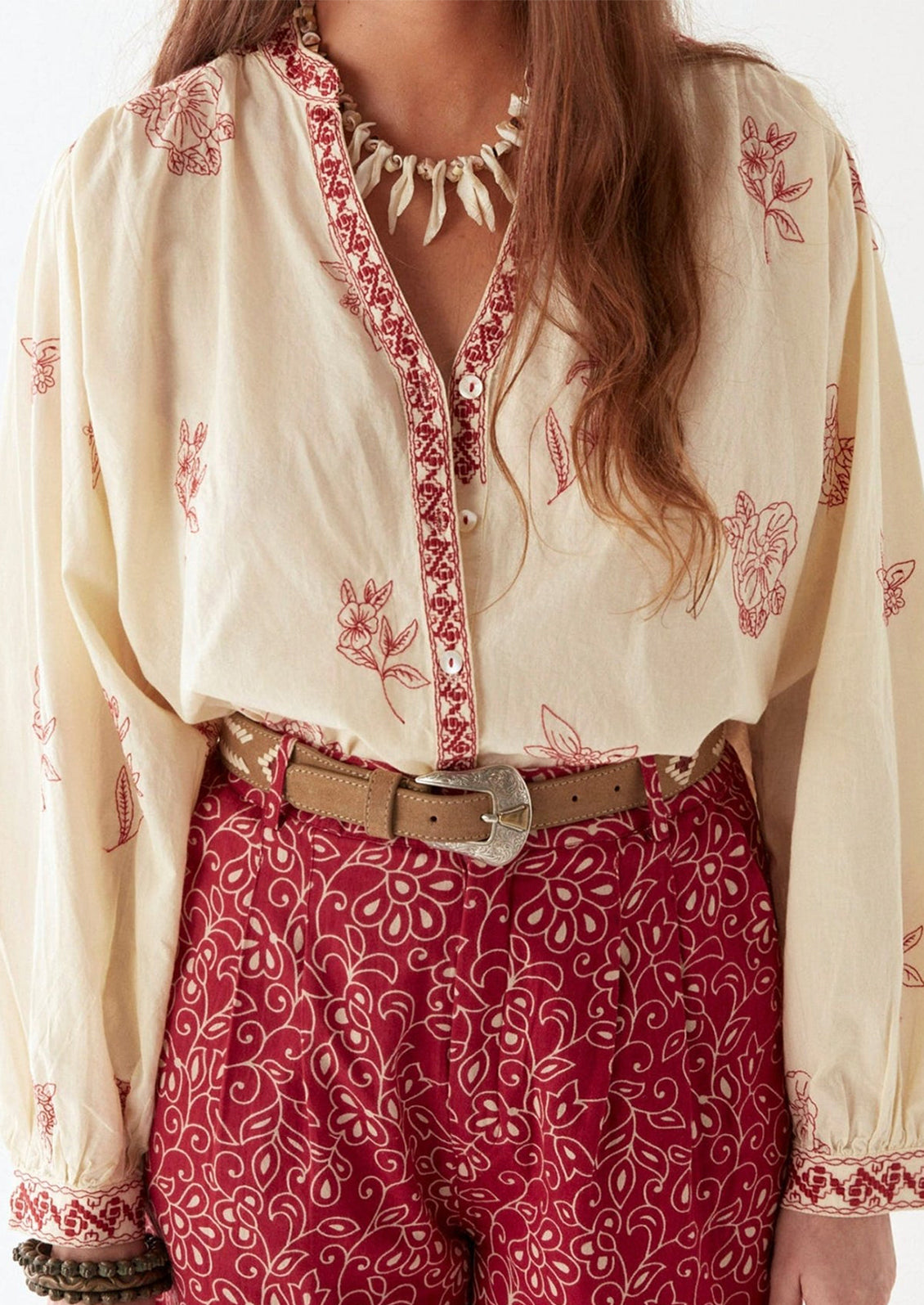 A person wearing a cream colored blouse with red floral embroidery.