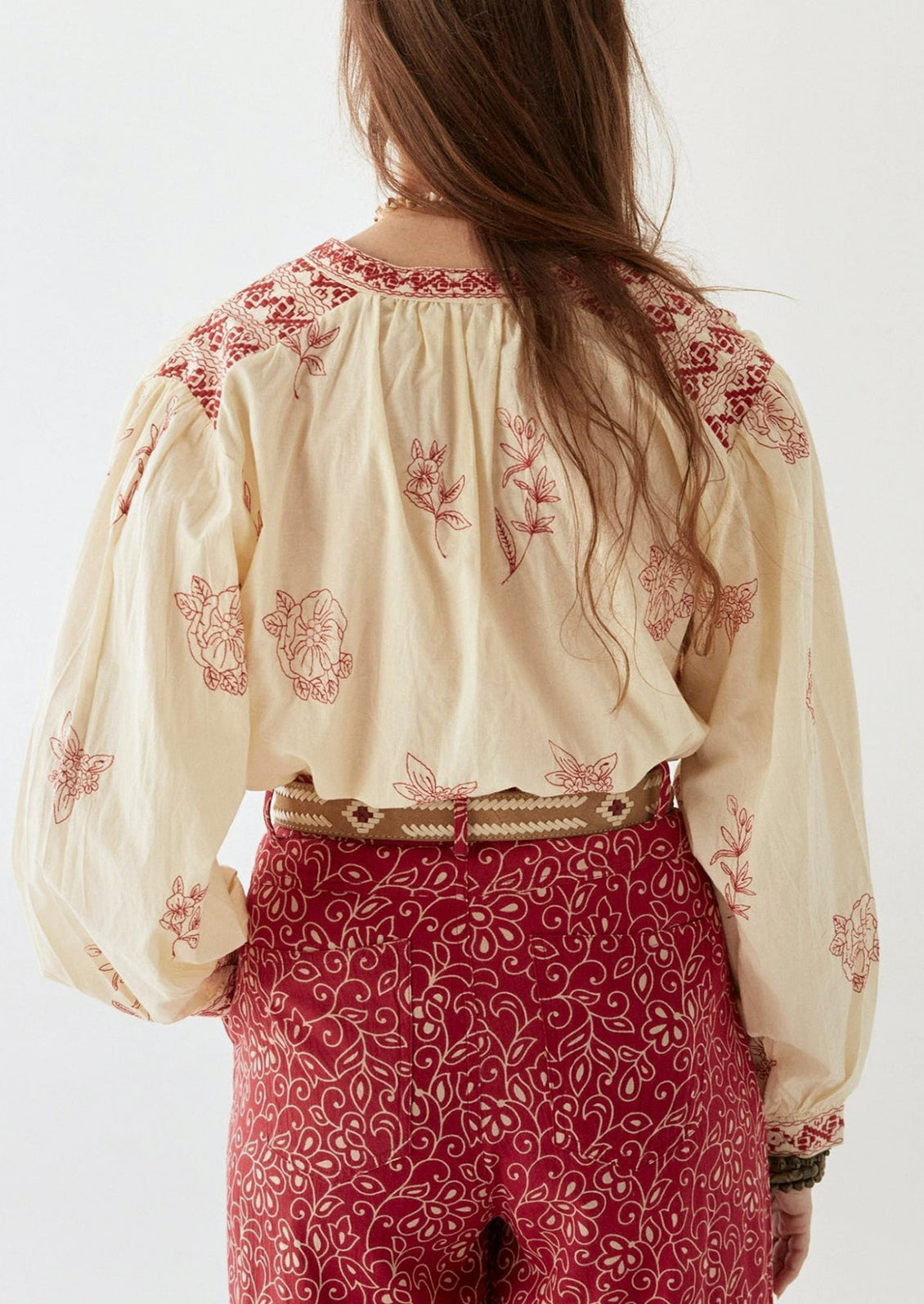 A person wearing a cream colored blouse with red floral embroidery.