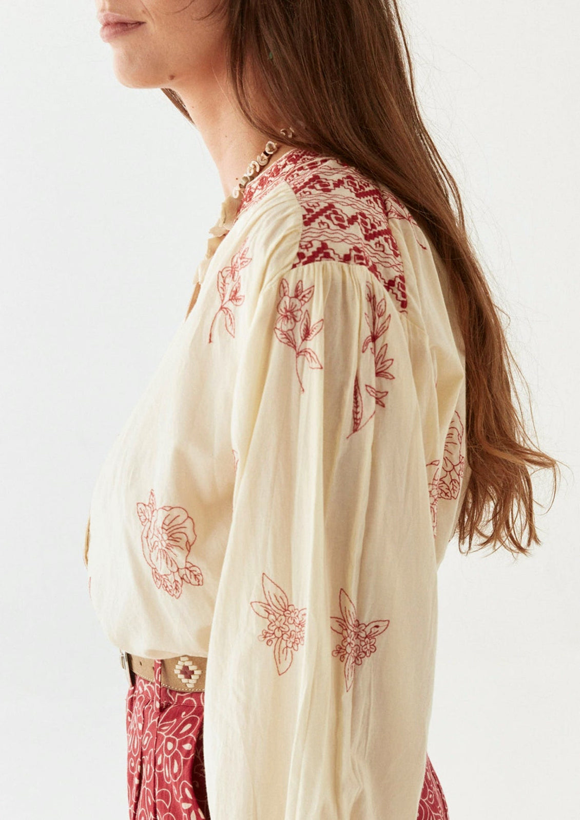 A person wearing a cream colored blouse with red floral embroidery.