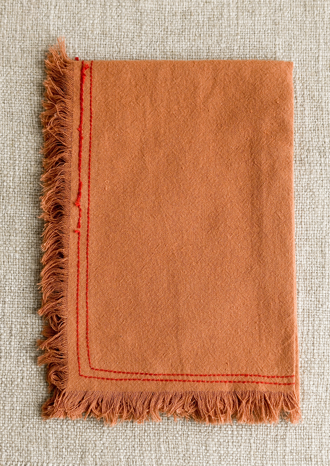 An orange tea towel with red stitching.
