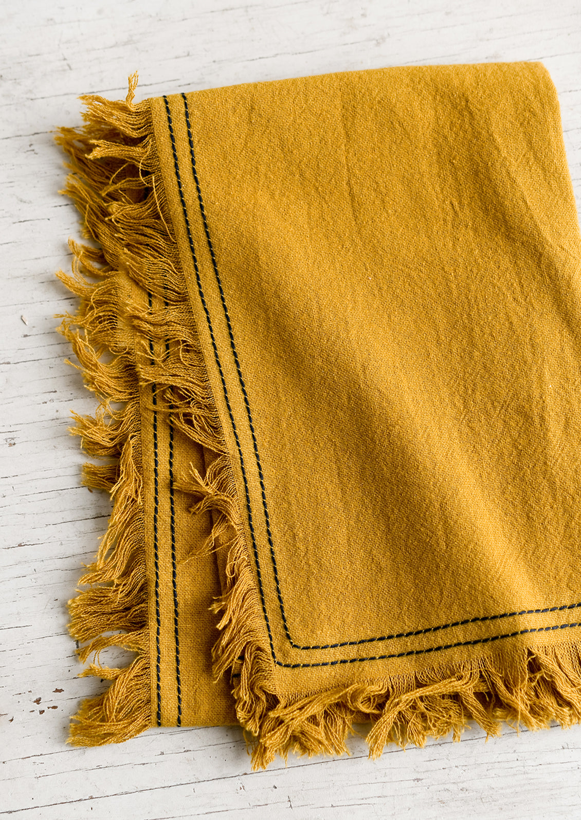 A mustard tea towel with navy stitching.