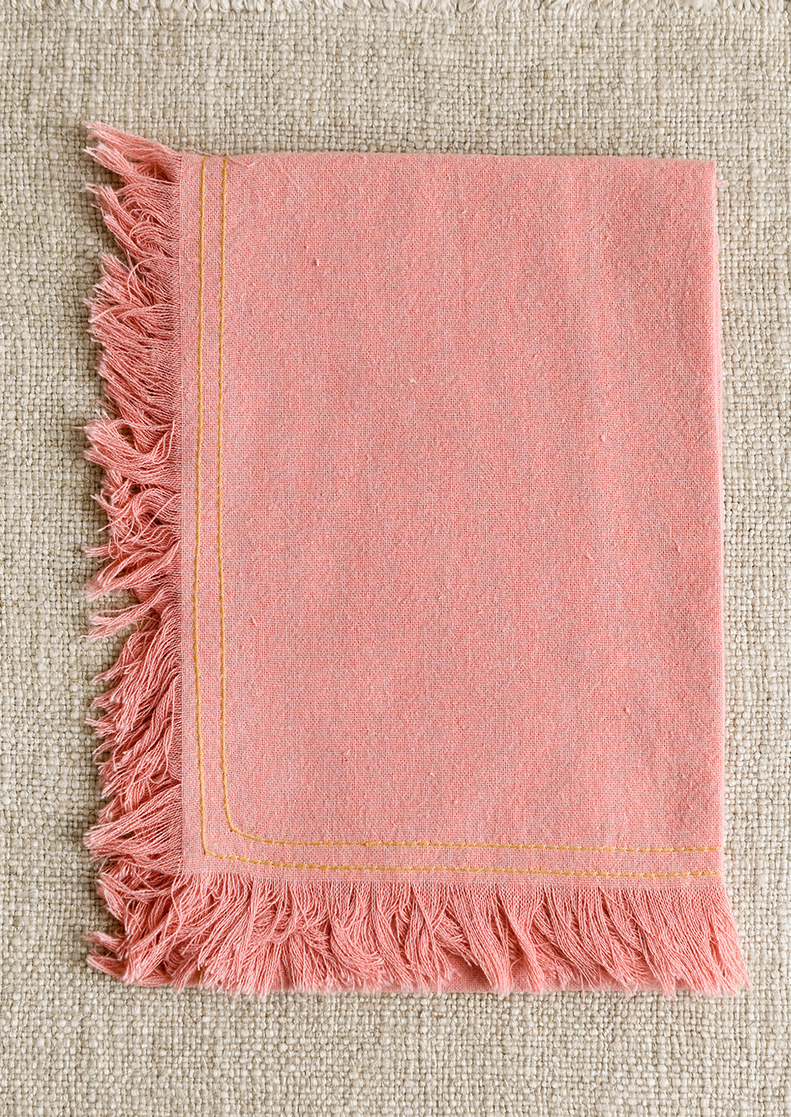 A pink tea towel with yellow stitching.