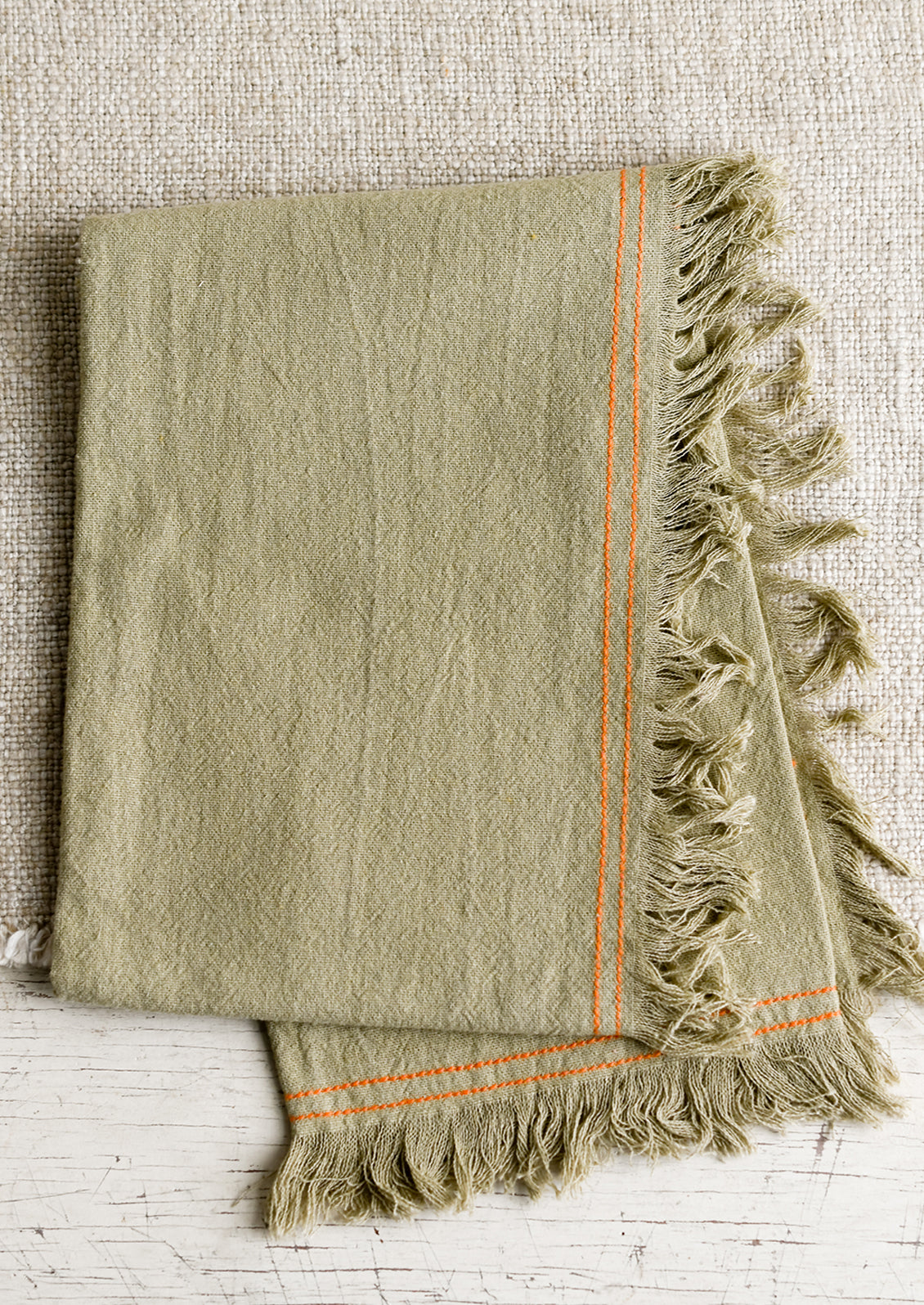 A green tea towel with orange stitching.