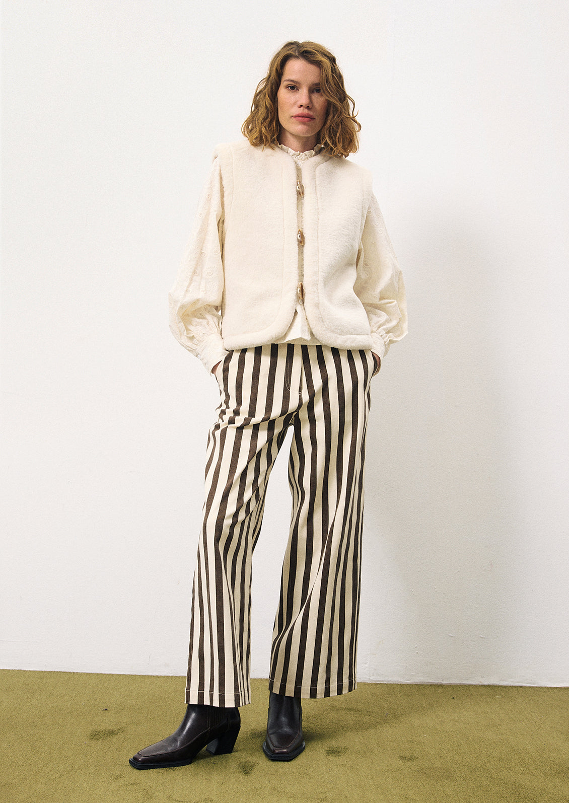 A woman wearing a pair of pants with thick vertical brown stripes on cream.