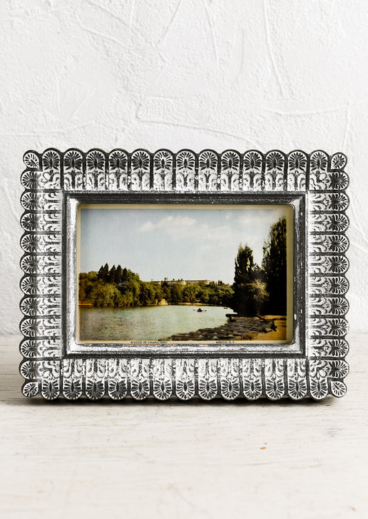 A picture frame with scalloped edges in dark grey with white paint wash.