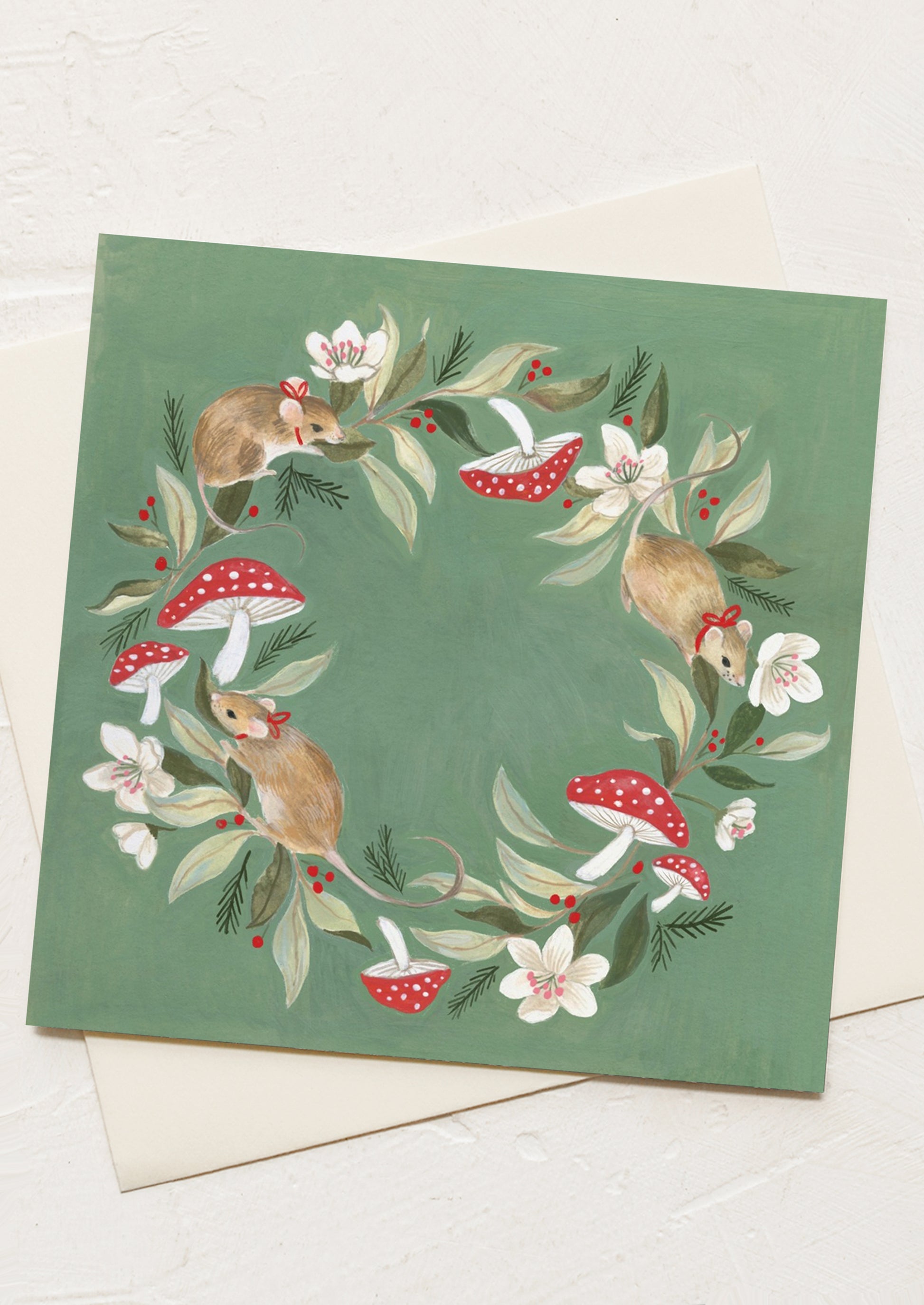 A greeting card with mice wearing red bowls dancing around mushroom wreath.