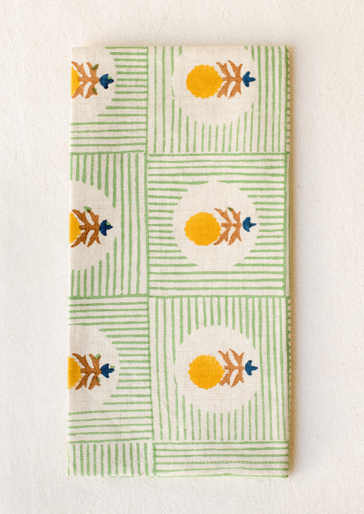 A block printed linen napkin in green stripe with yellow and brown floral.