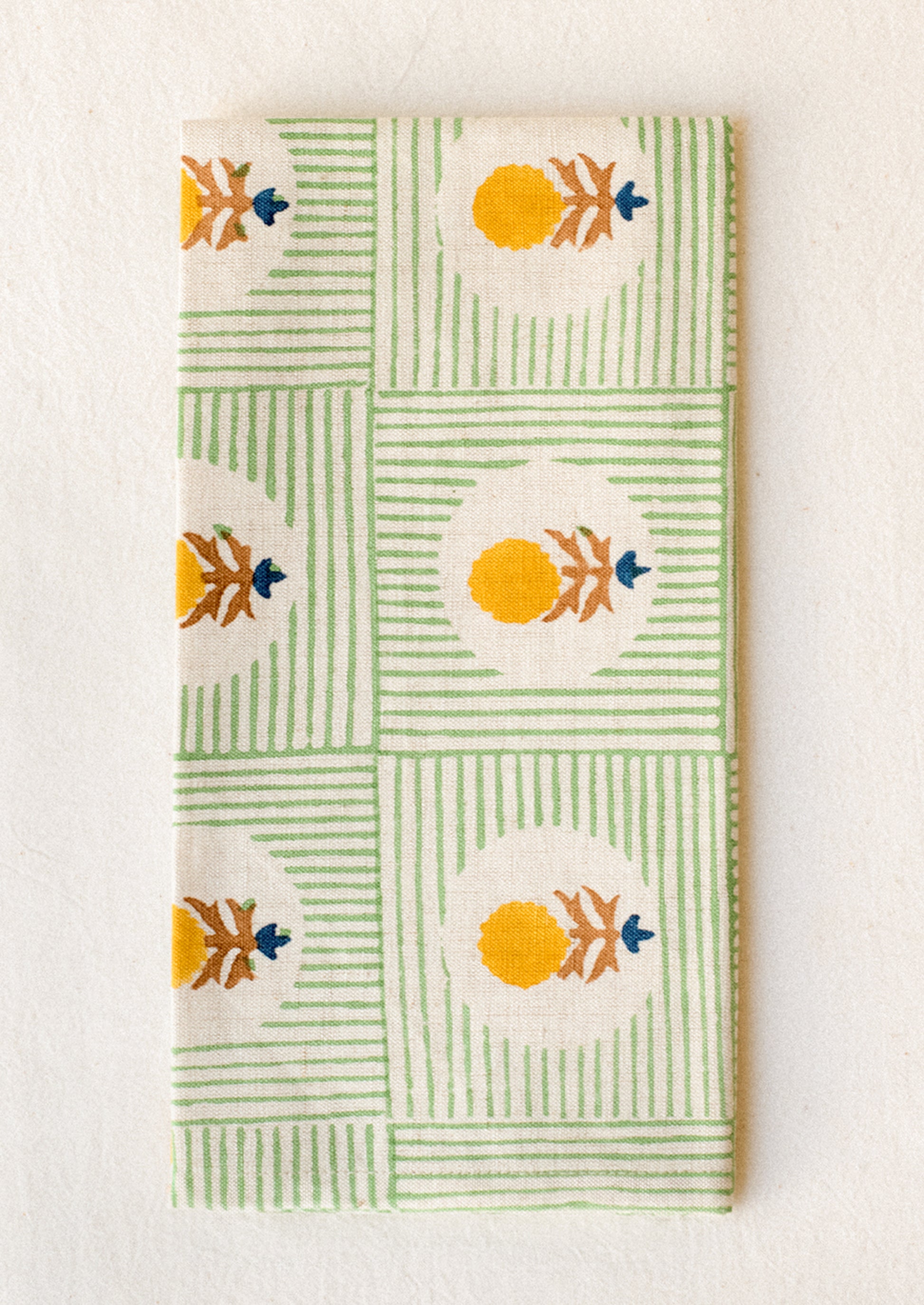 A block printed linen napkin in green stripe with yellow and brown floral.