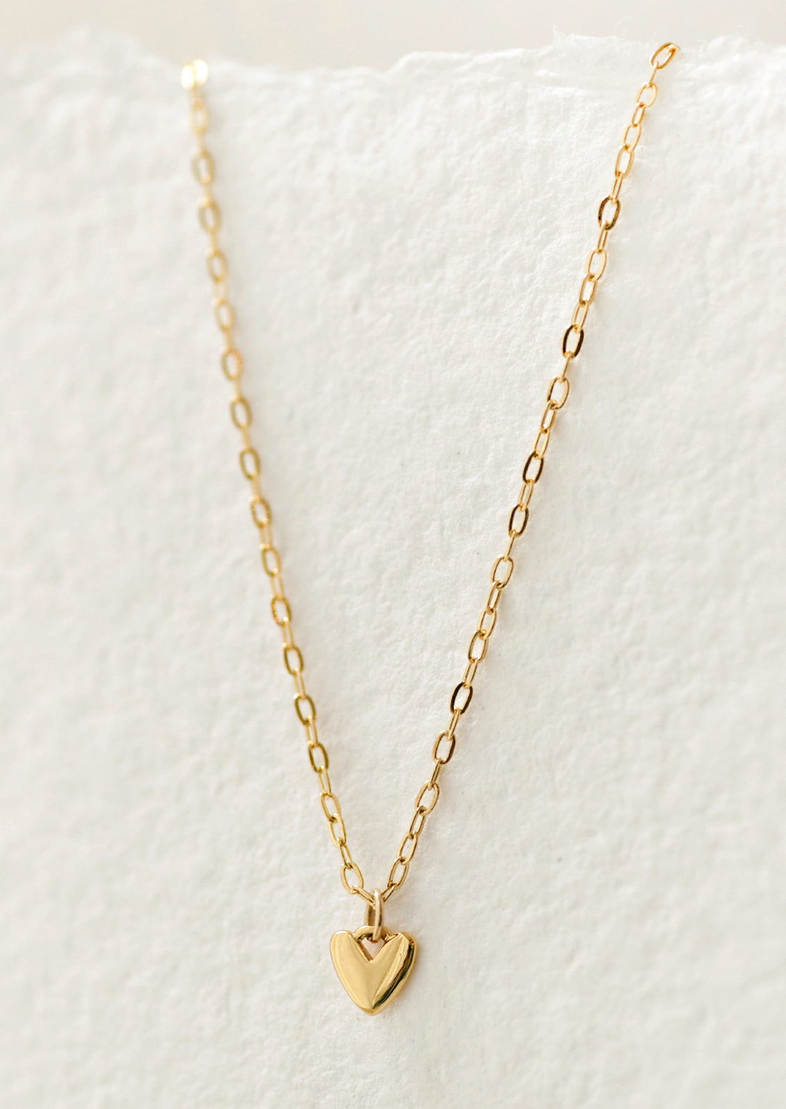 A gold chain necklace with a mini heart charm.