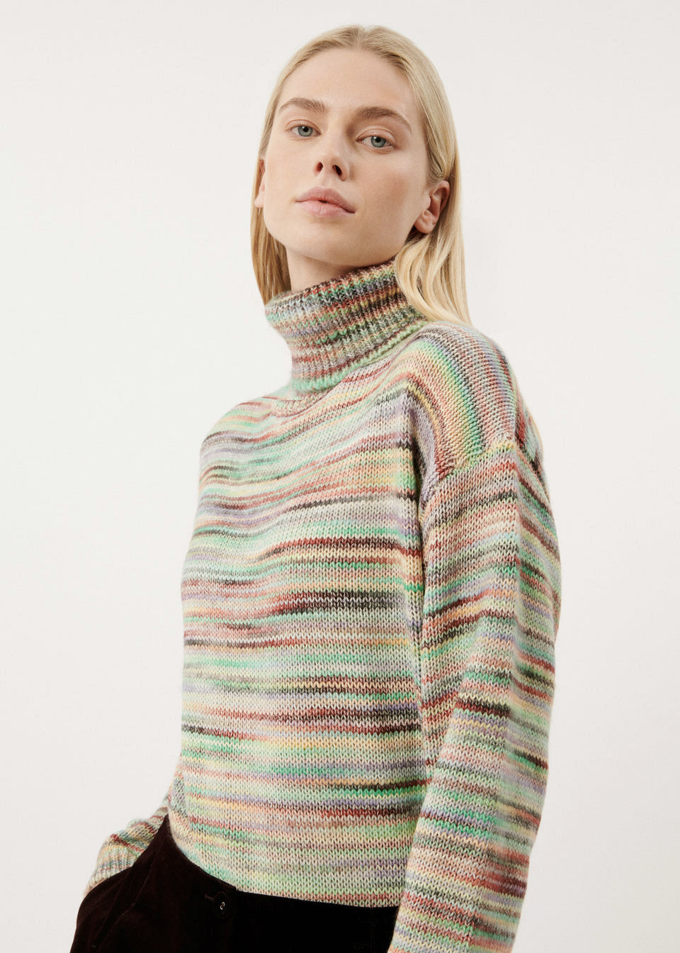 A woman wearing a turtleneck sweater in multicolor spacedye knit.