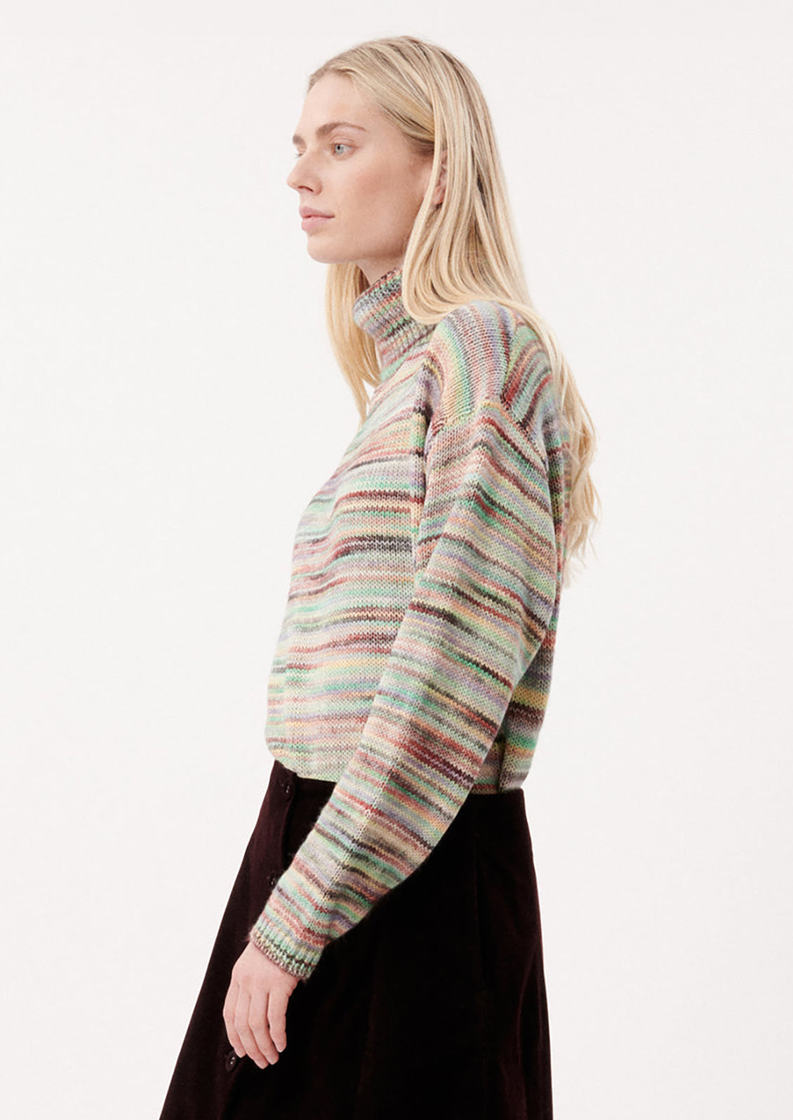 A woman wearing a turtleneck sweater in multicolor spacedye knit.