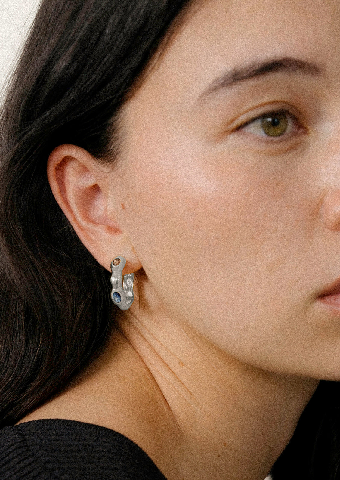 A woman wearing a sterling silver earring with various colored gemstones.