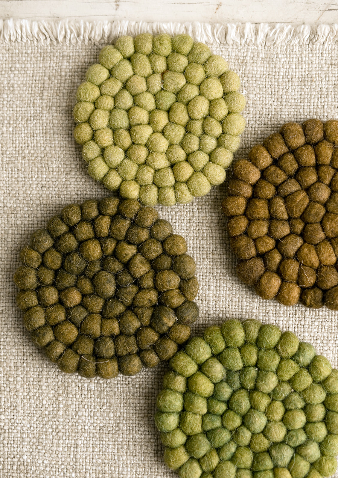 A set of felted ball coasters in mixed tones of green.