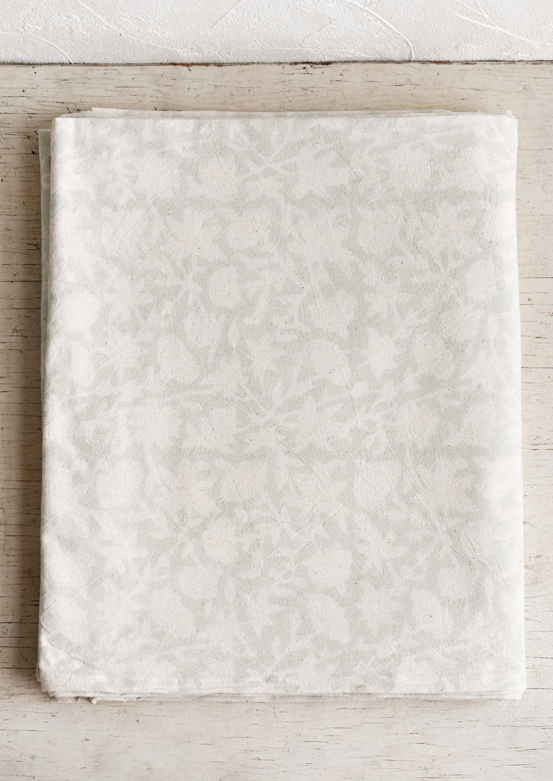 A block printed tablecloth in white floral print on very light seafoam background.
