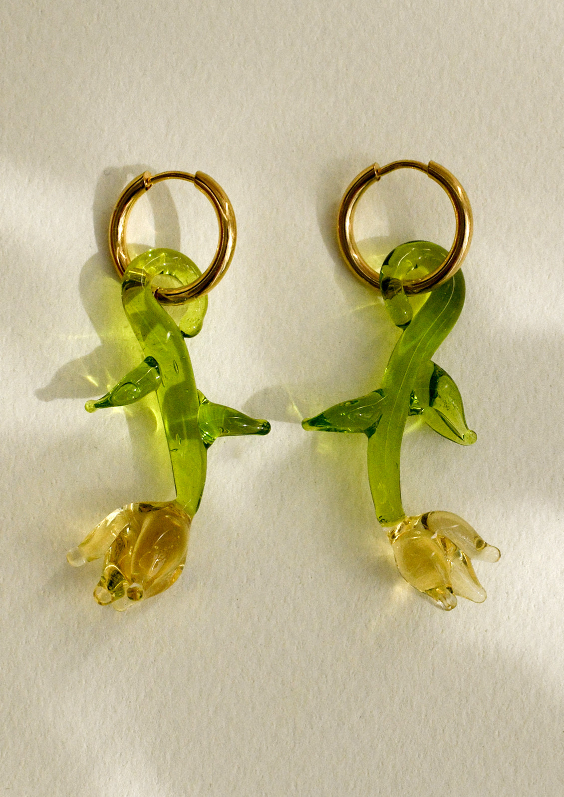 A pair of gold hoop earrings with murano glass yellow tulip charm.