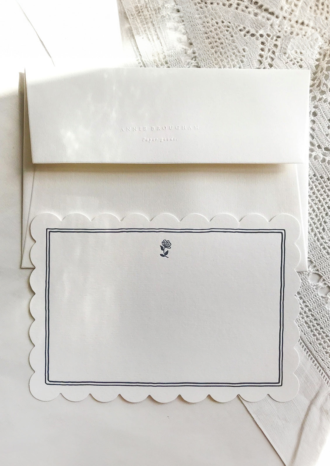 A scalloped white notecard with navy border and white envelope.