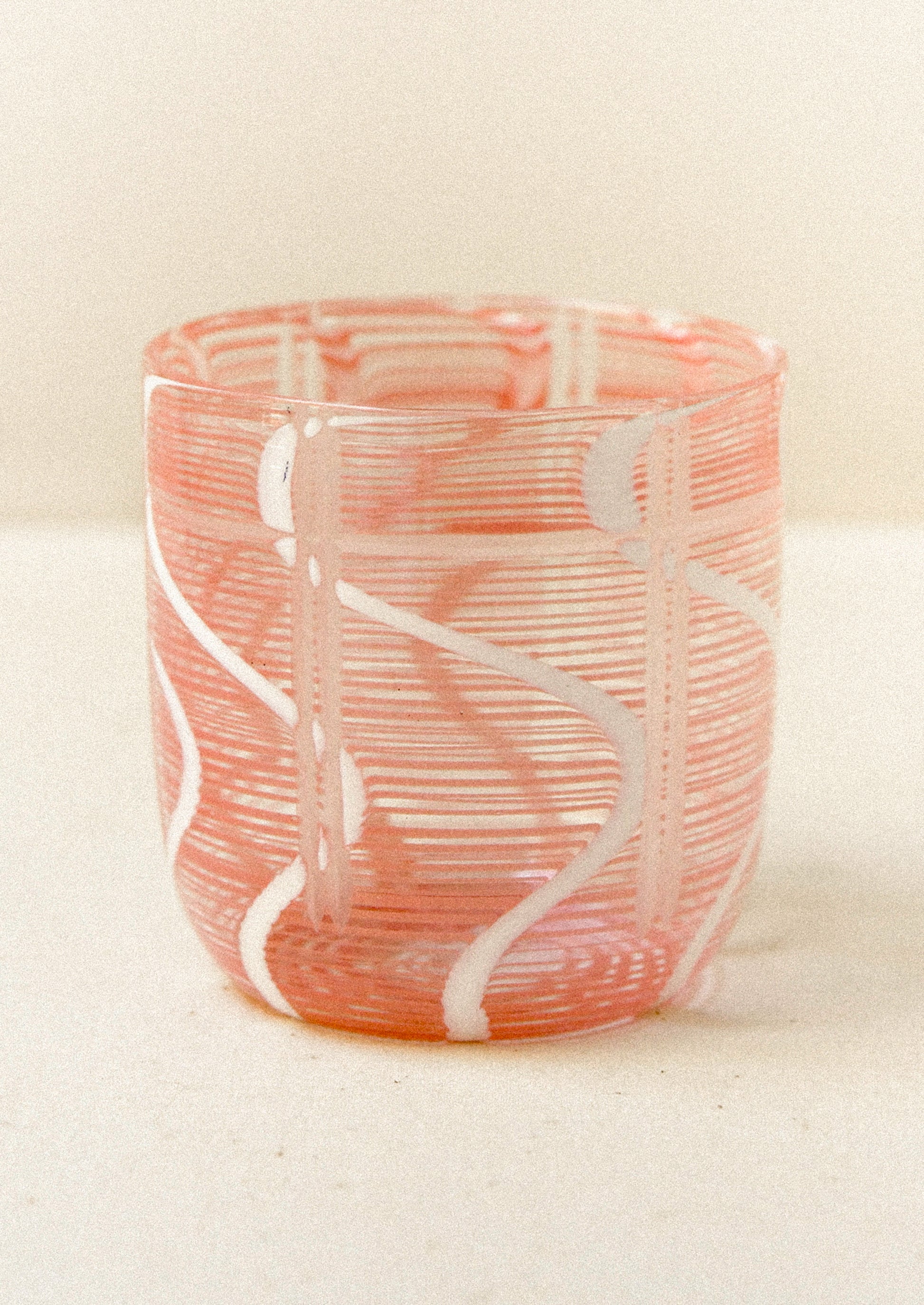 Pink glass with white swirl patterns on a beige background