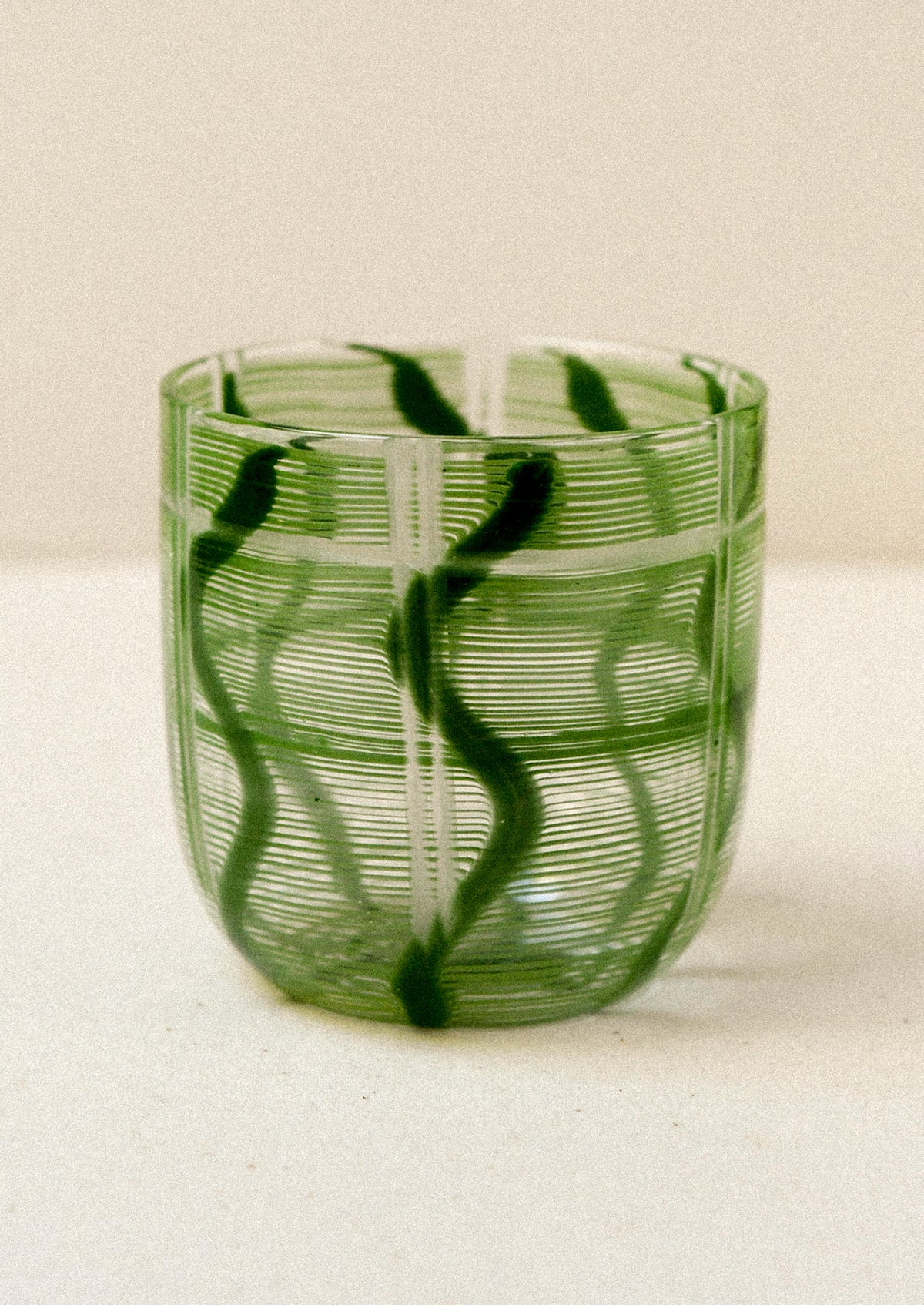 Green glass tumbler with wavy pattern on a white background