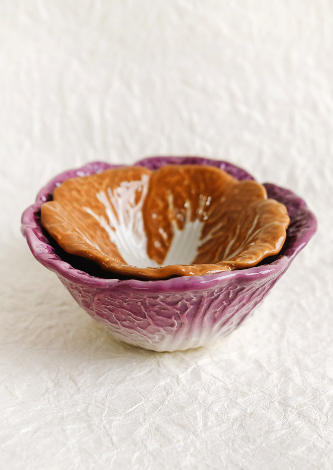 A pair of ceramic nesting bowls that look like orange and purple cabbage.