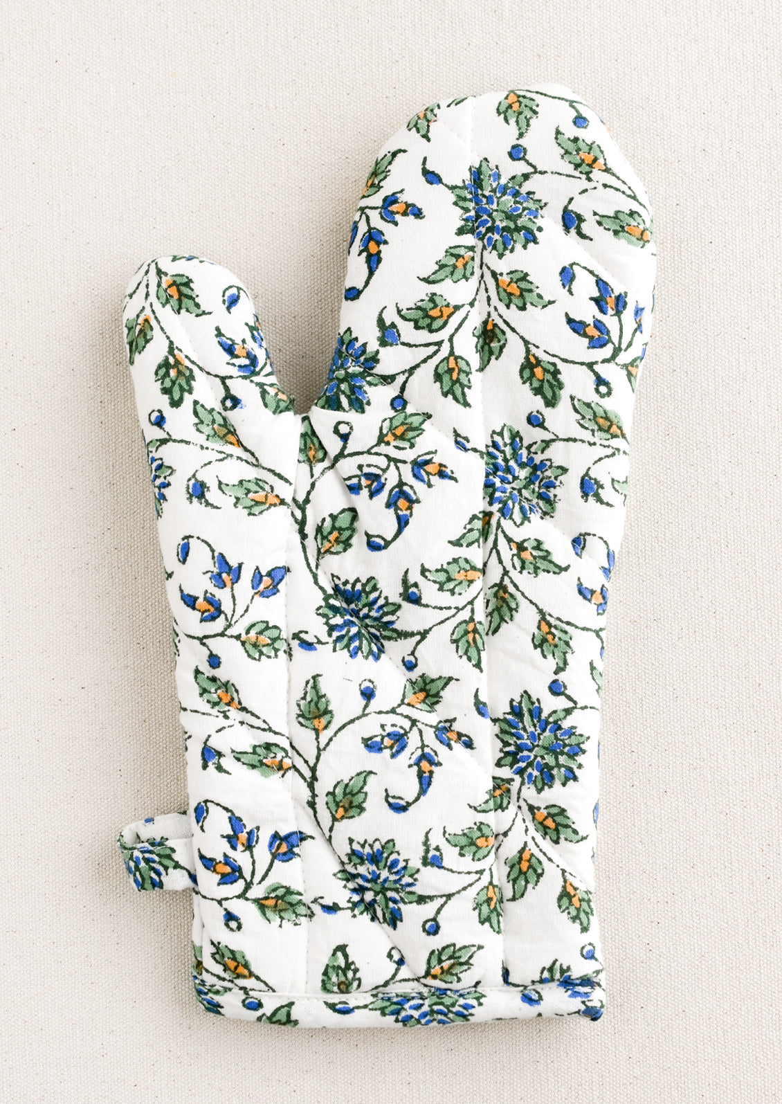 A quilted white cotton oven mitt with blue, green and orange floral pattern.