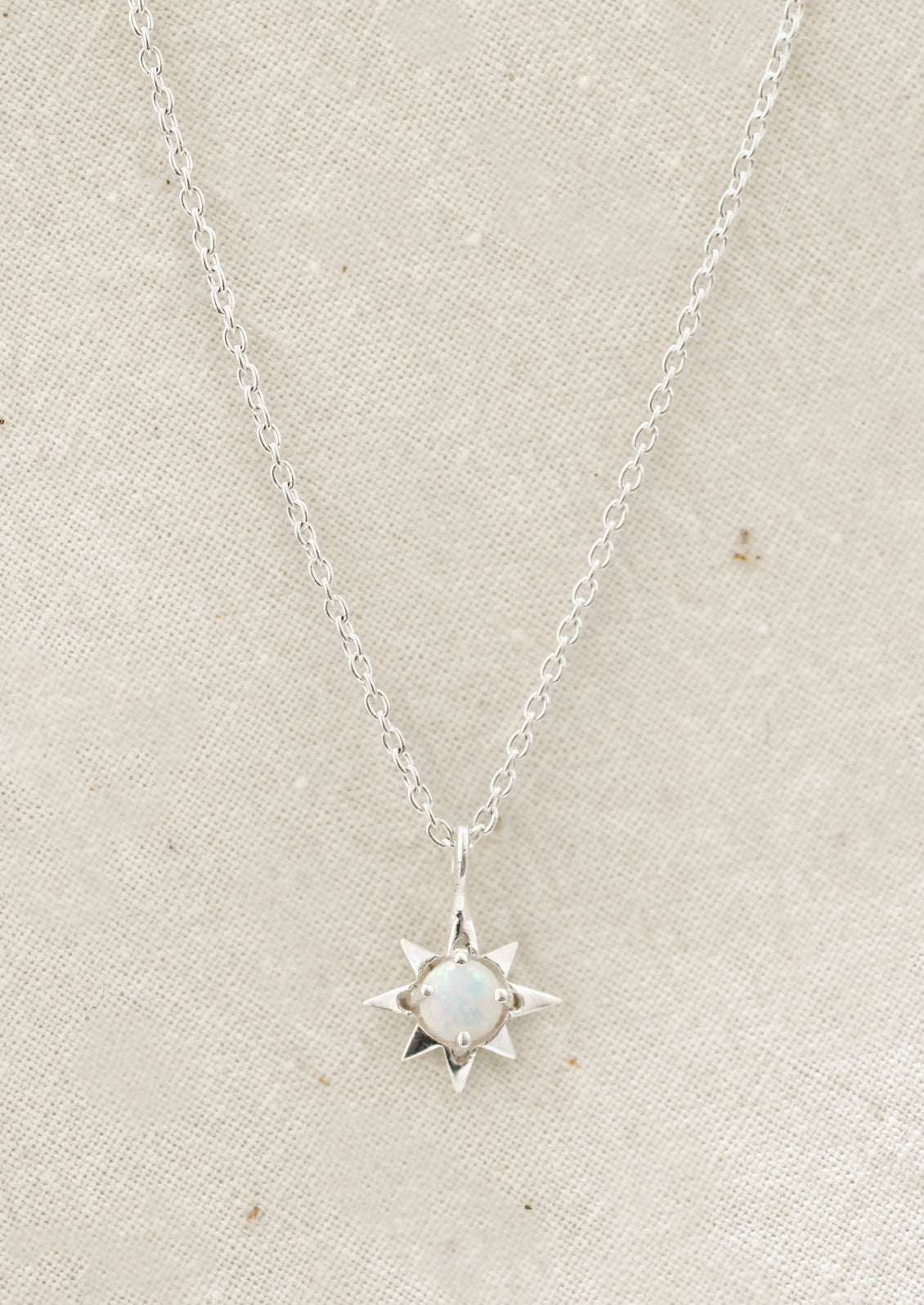 A sterling silver necklace with a north star shaped charm with an opal in the center.