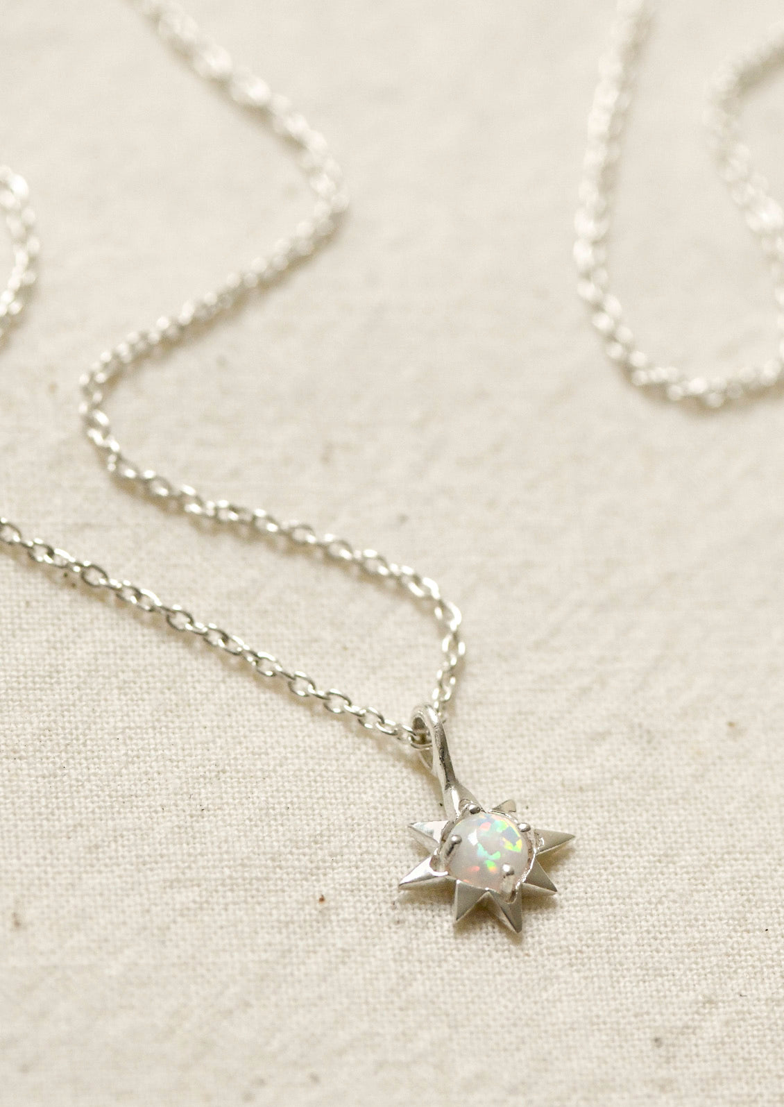 A sterling silver necklace with a north star shaped charm with an opal in the center.