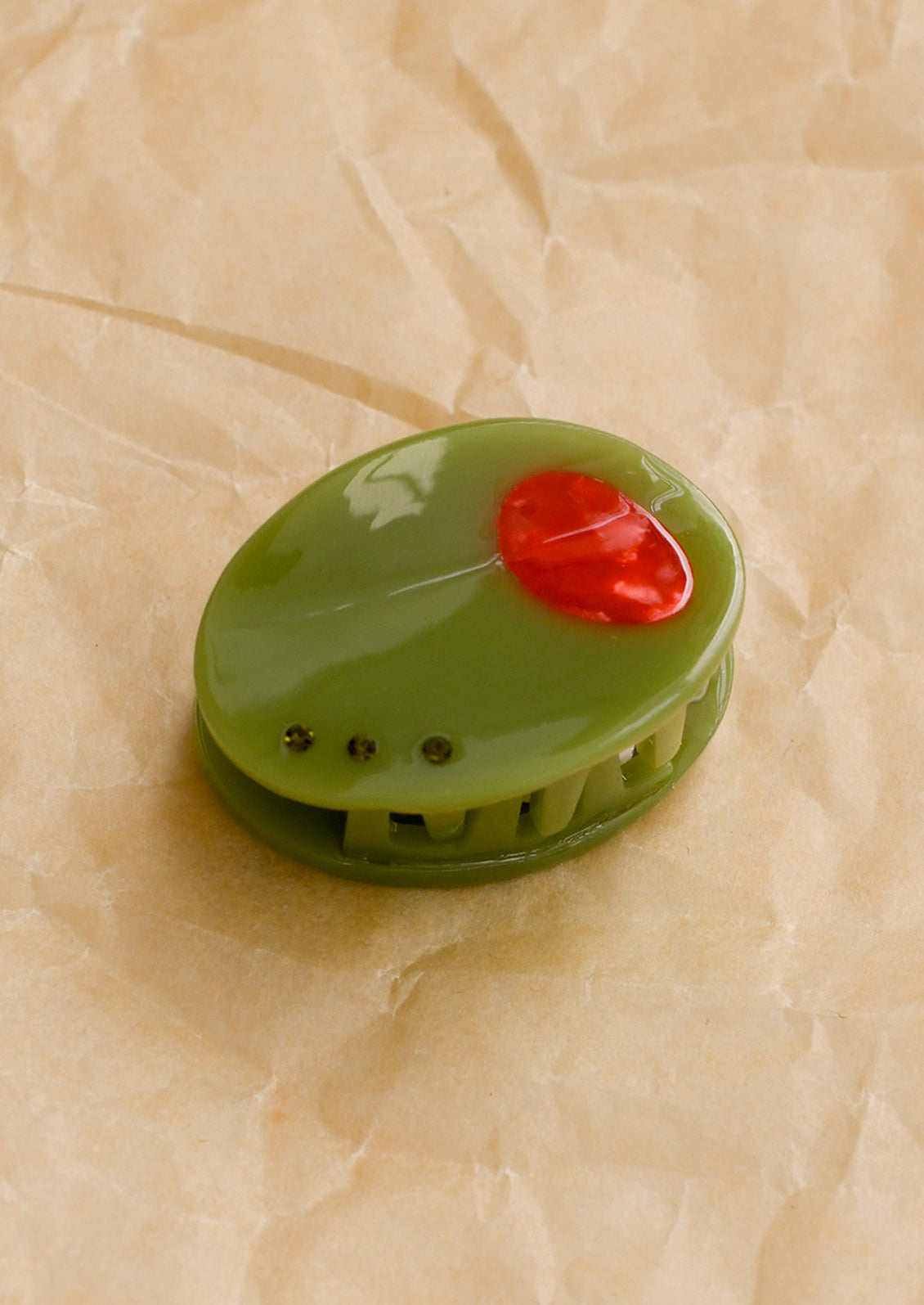 A small hair claw in the shape of a green olive with red detailing.