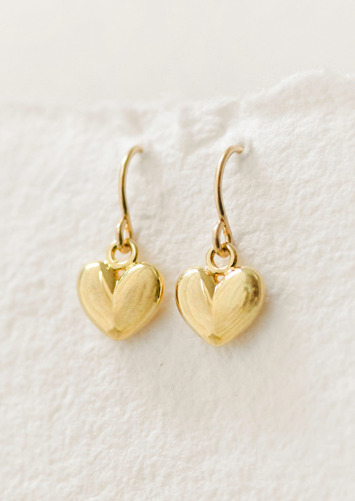 A pair of gold puffy heart dangling earrings.