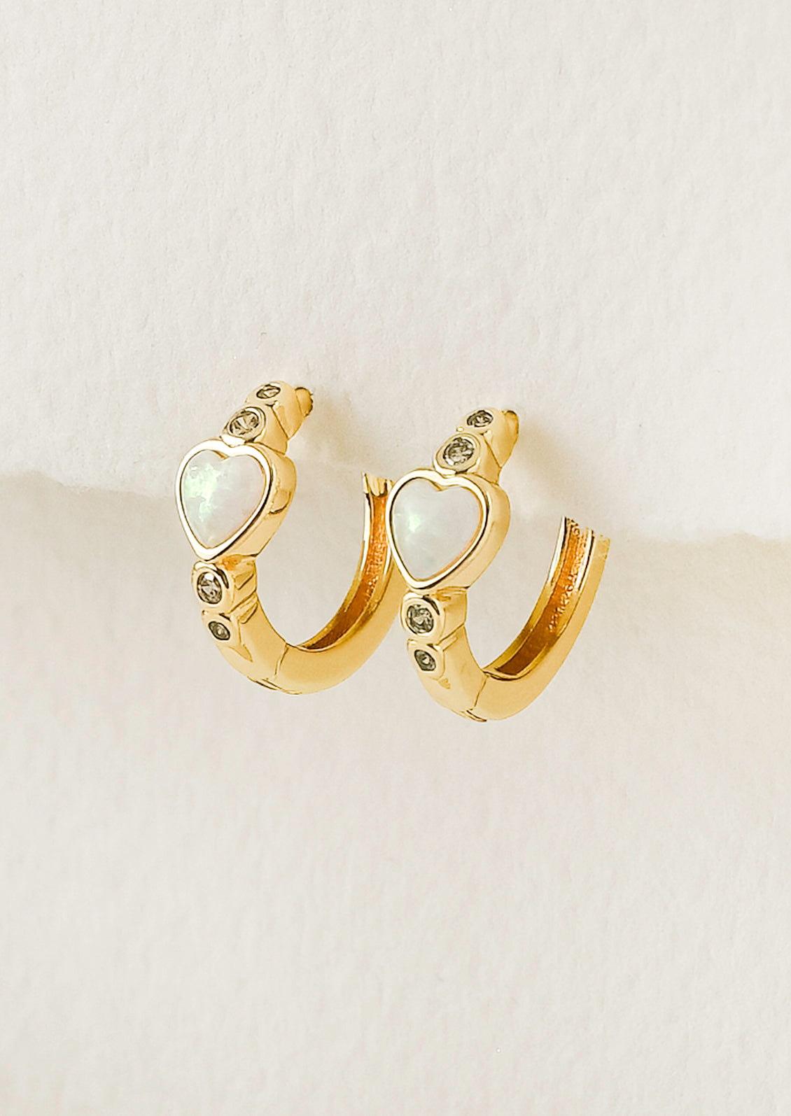 A pair of gold hoop earrings with a heart=shaped opal in the center and tiny gems above and below.
