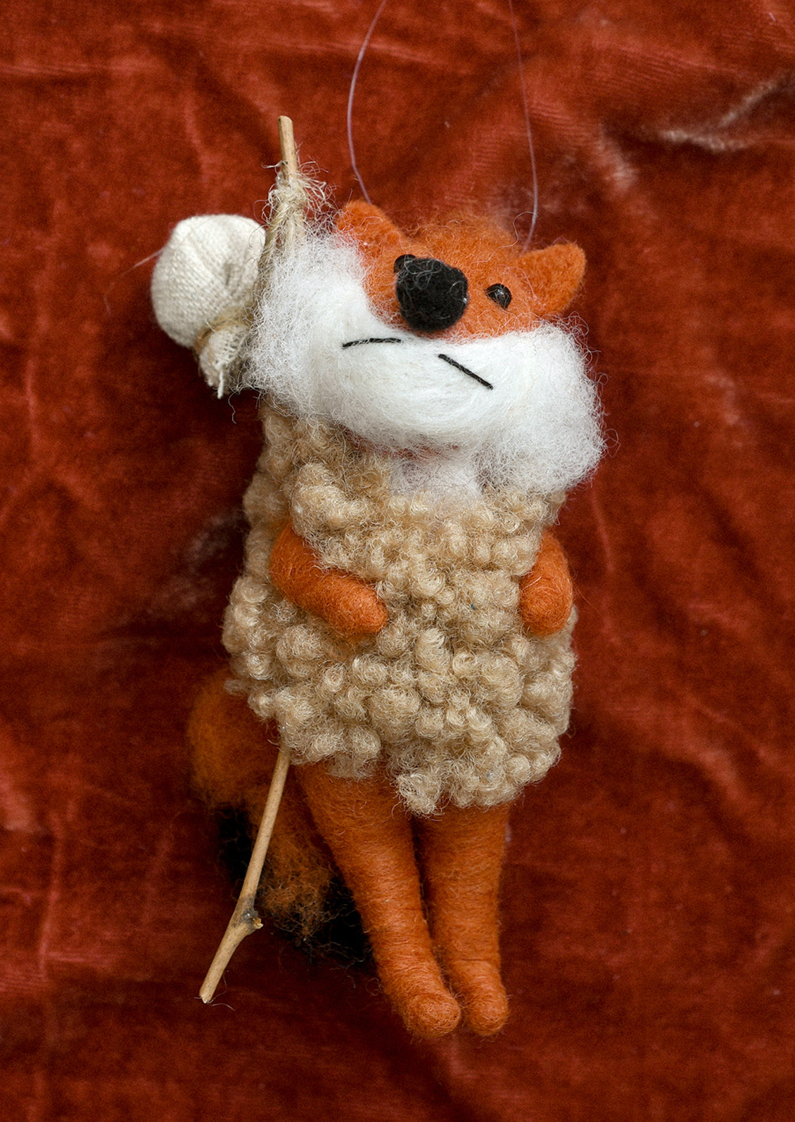 A felted wool ornament of fox carrying hiker pole.