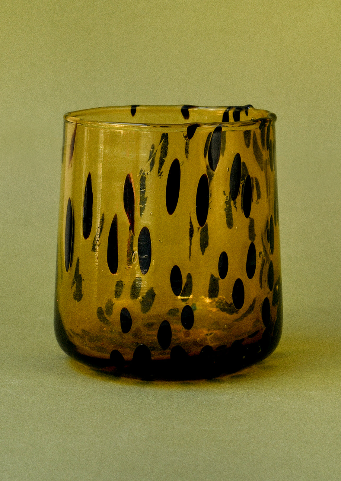 A dark yellow drinking glass with black abstract spots.