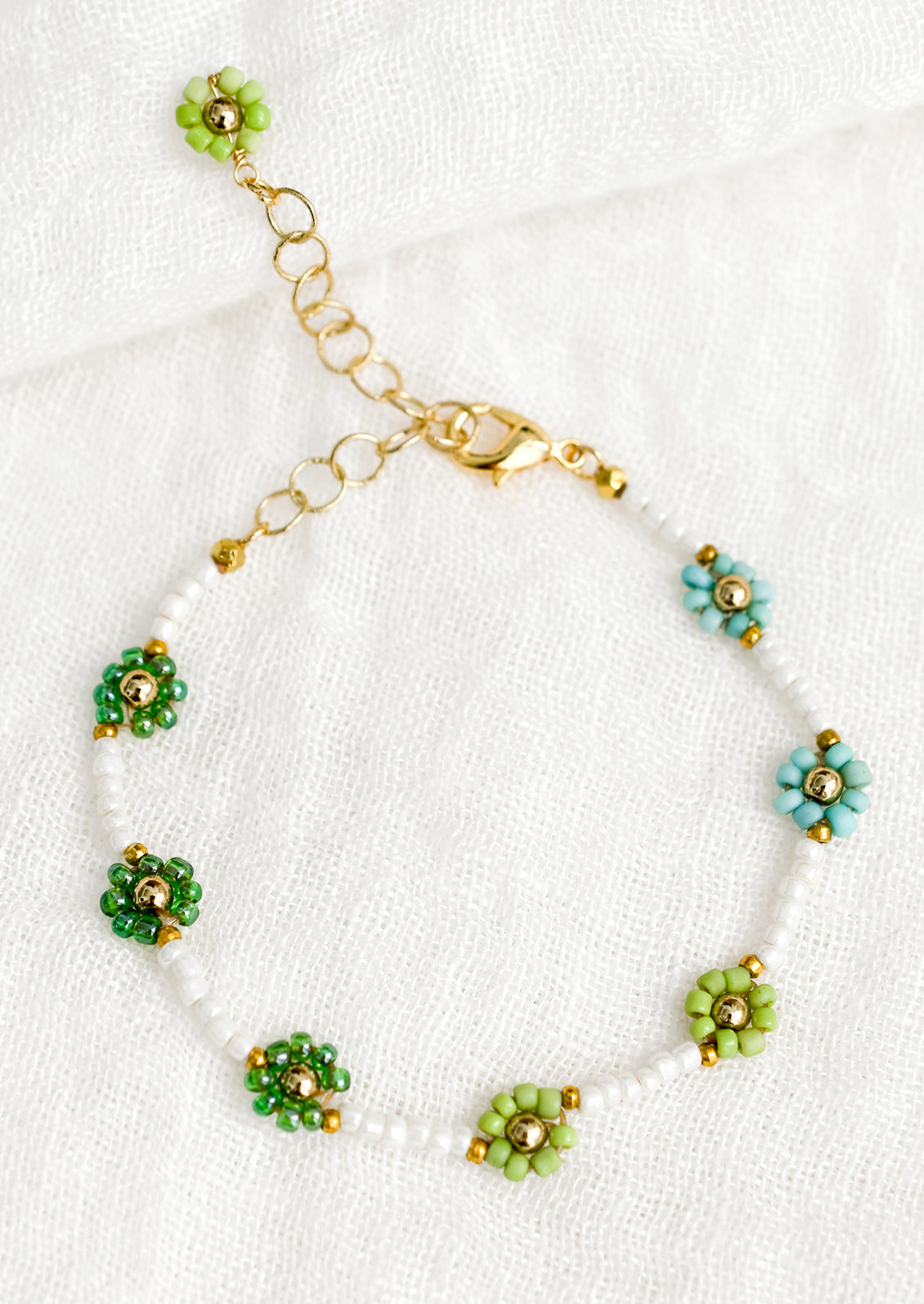 A white beaded bracelet with green and turquoise beaded flowers.