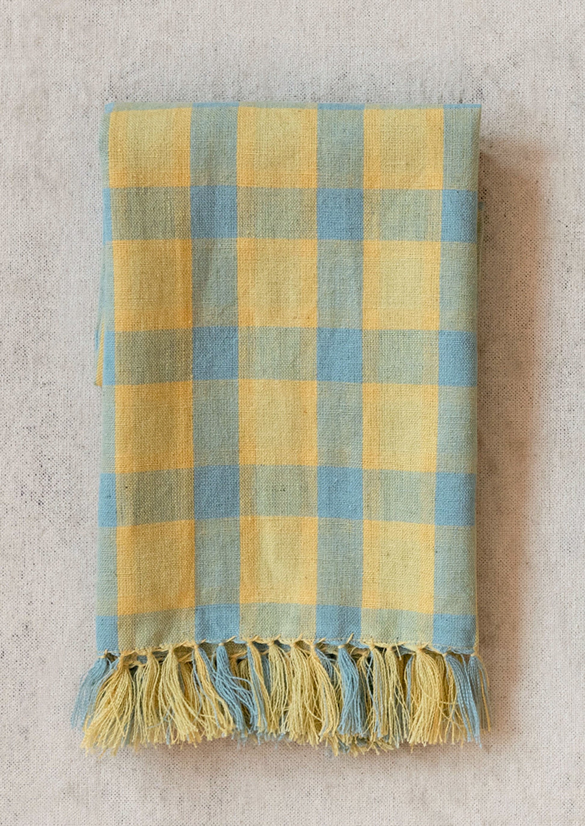 A cotton-linen tea towel in blue and yellow check pattern with tassel trim.