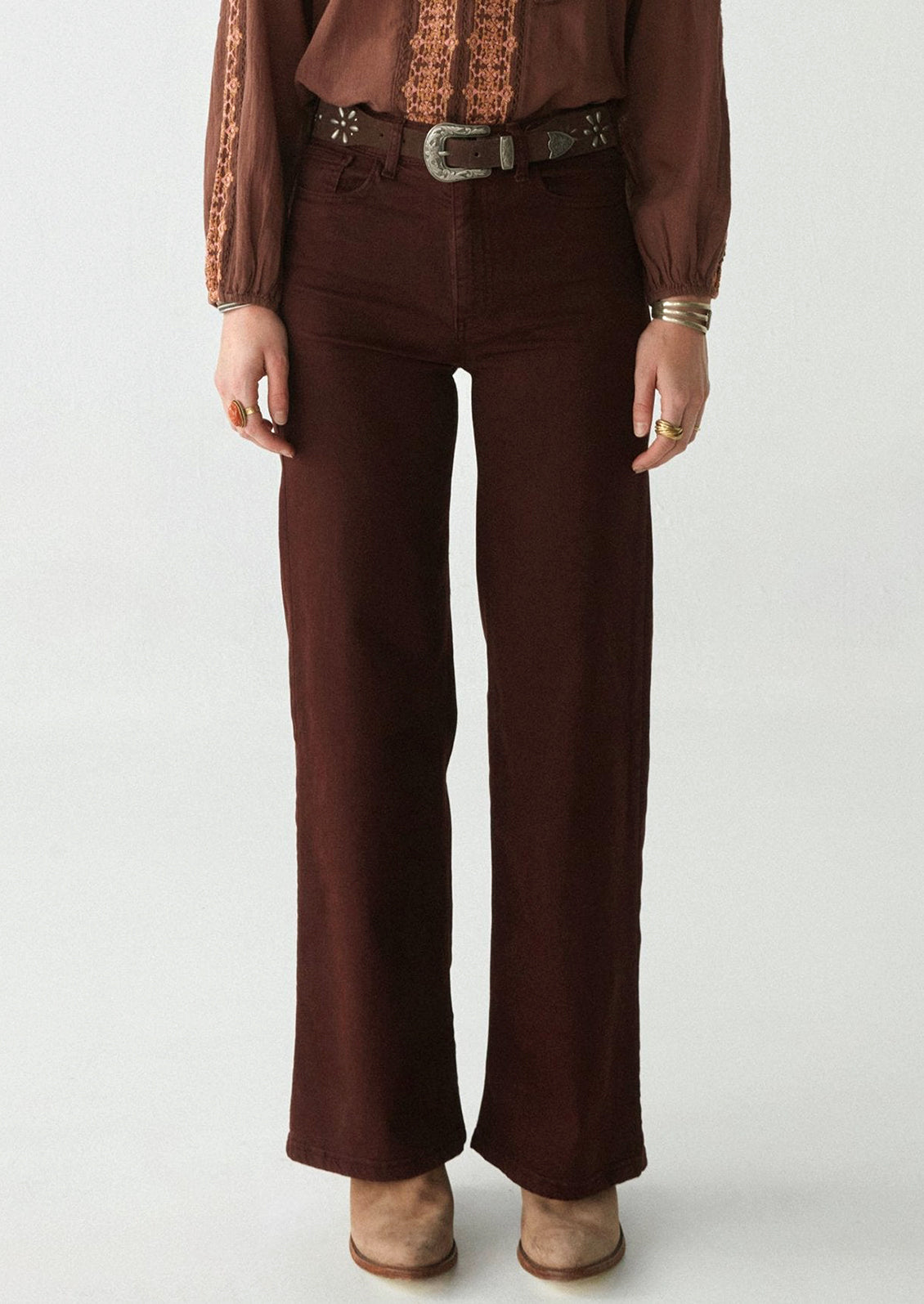 A woman wearing a pair of form fitting, straight leg pants in dark brown.