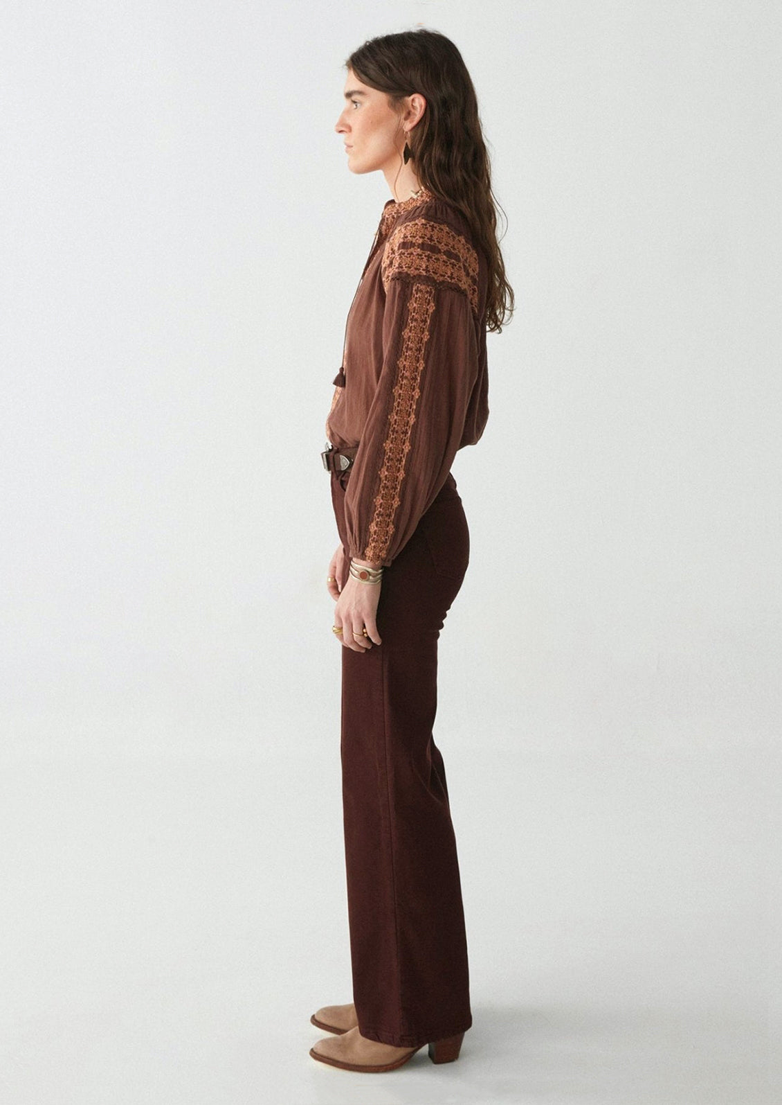 A woman wearing a pair of form fitting, straight leg pants in dark brown.