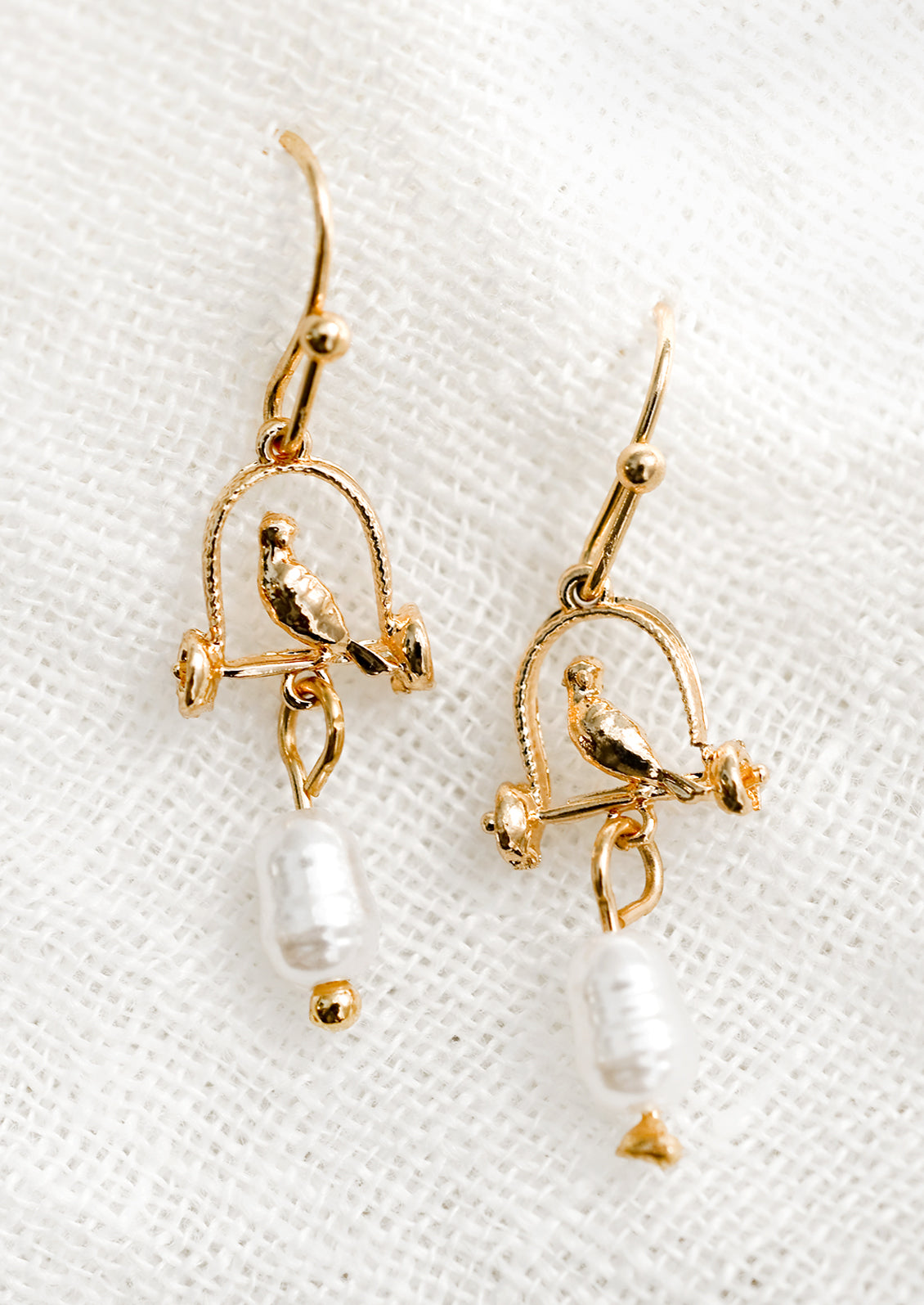 A pair of gold earrings depicting bird sitting on perch, with pearl bead.