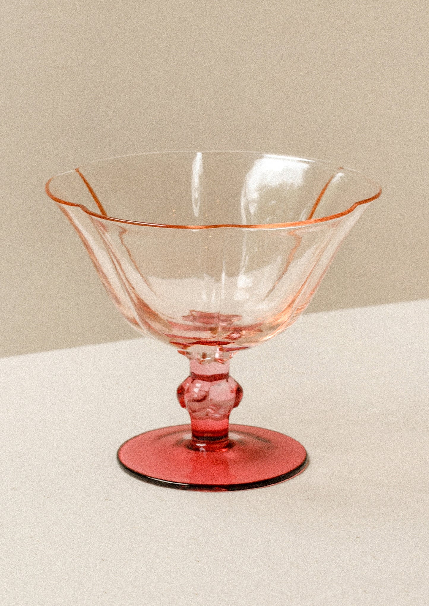 A short coupe glass with peach top and fuchsia stem.