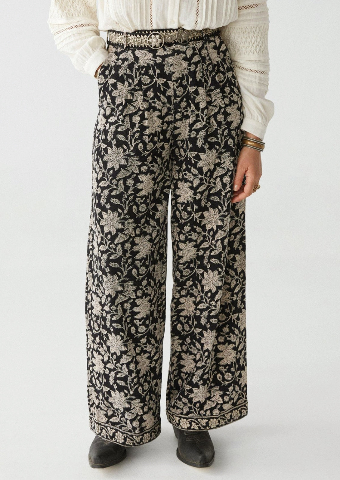 A woman wearing a pair of paisley floral print corduroy pants in black with white flowers.