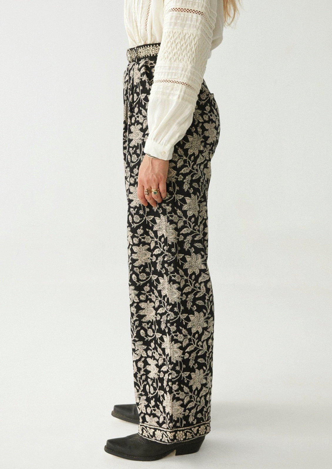 A woman wearing a pair of paisley floral print corduroy pants in black with white flowers.