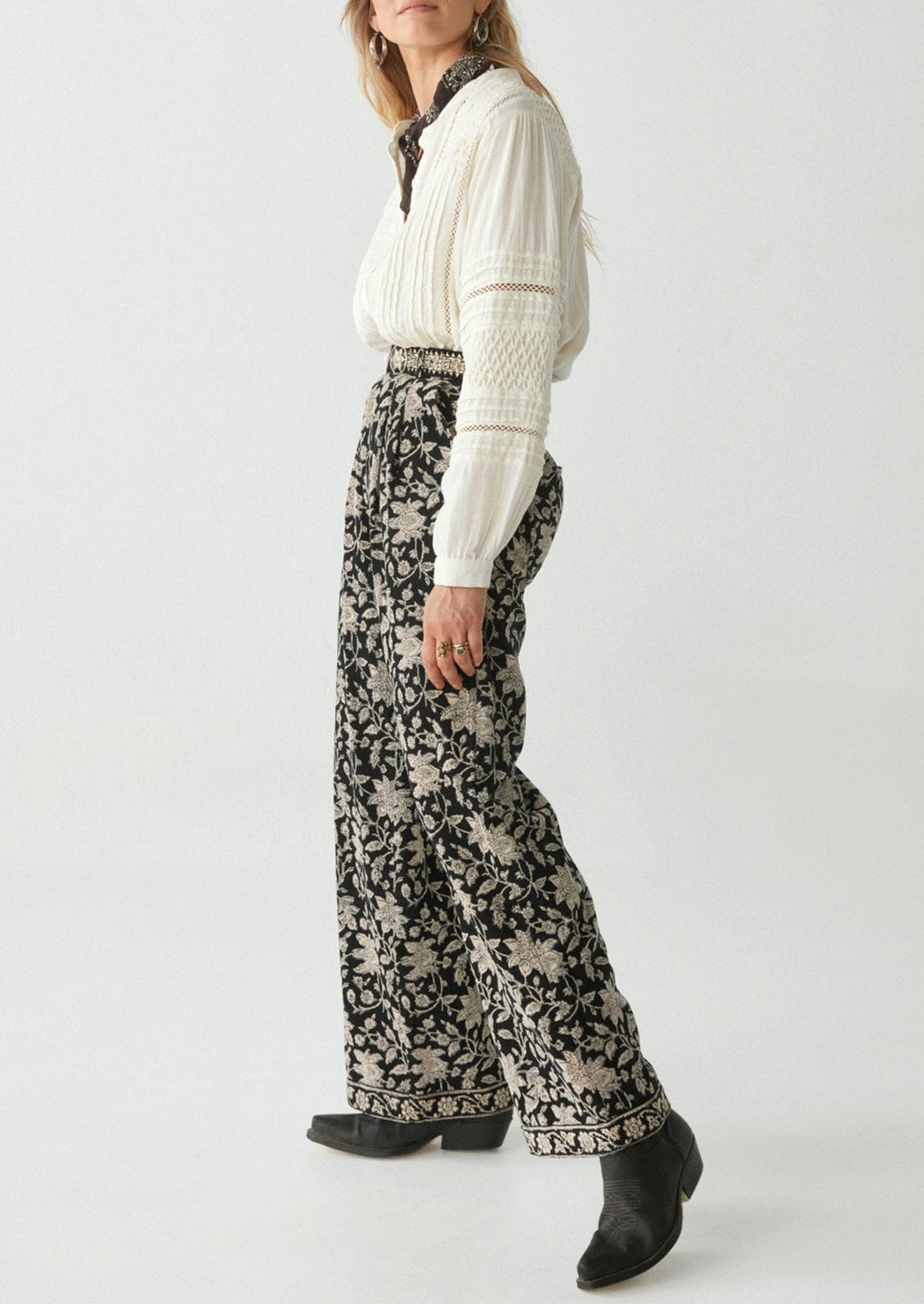 A woman wearing a pair of paisley floral print corduroy pants in black with white flowers.
