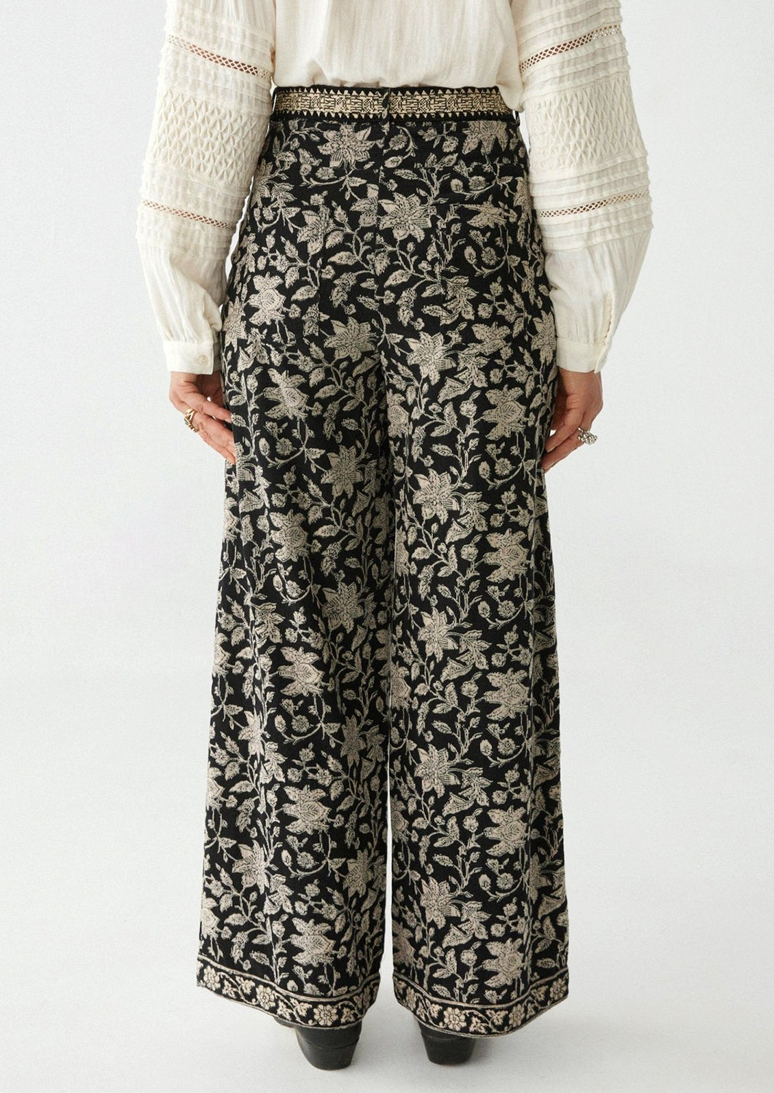 A woman wearing a pair of paisley floral print corduroy pants in black with white flowers.