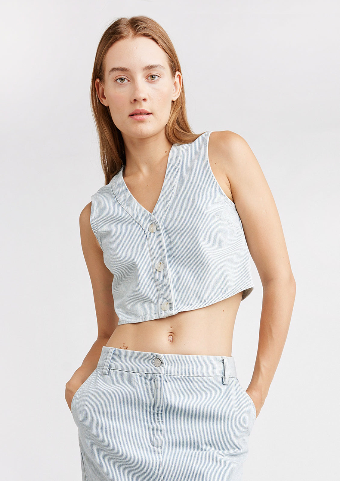 A woman wearing a v-neck crop top vest with light blue pinstripe pattern.