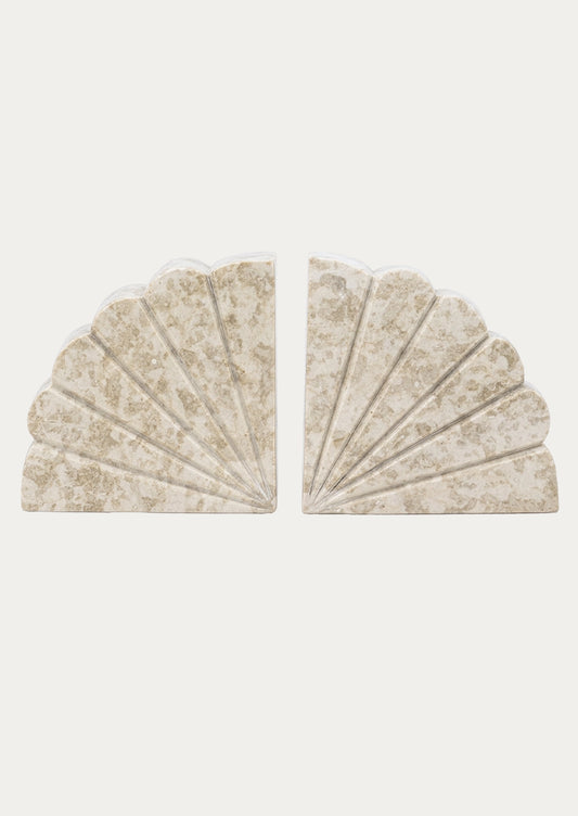 A pair of scalloped fan-shaped bookends made from a textured beige stone with subtle gold veining, displayed against a solid off-white background.