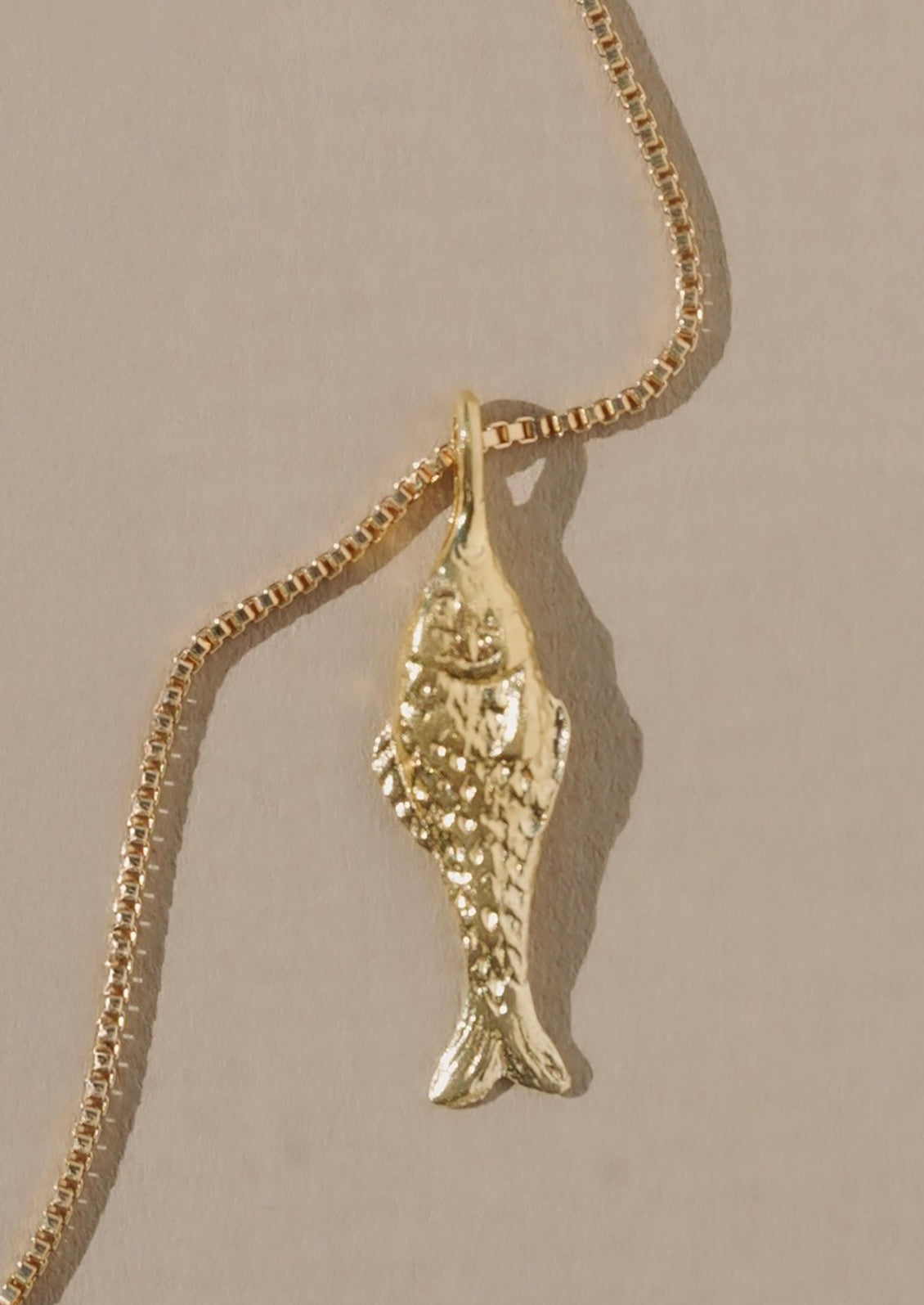 A gold necklace with fish charm on thin box chain.