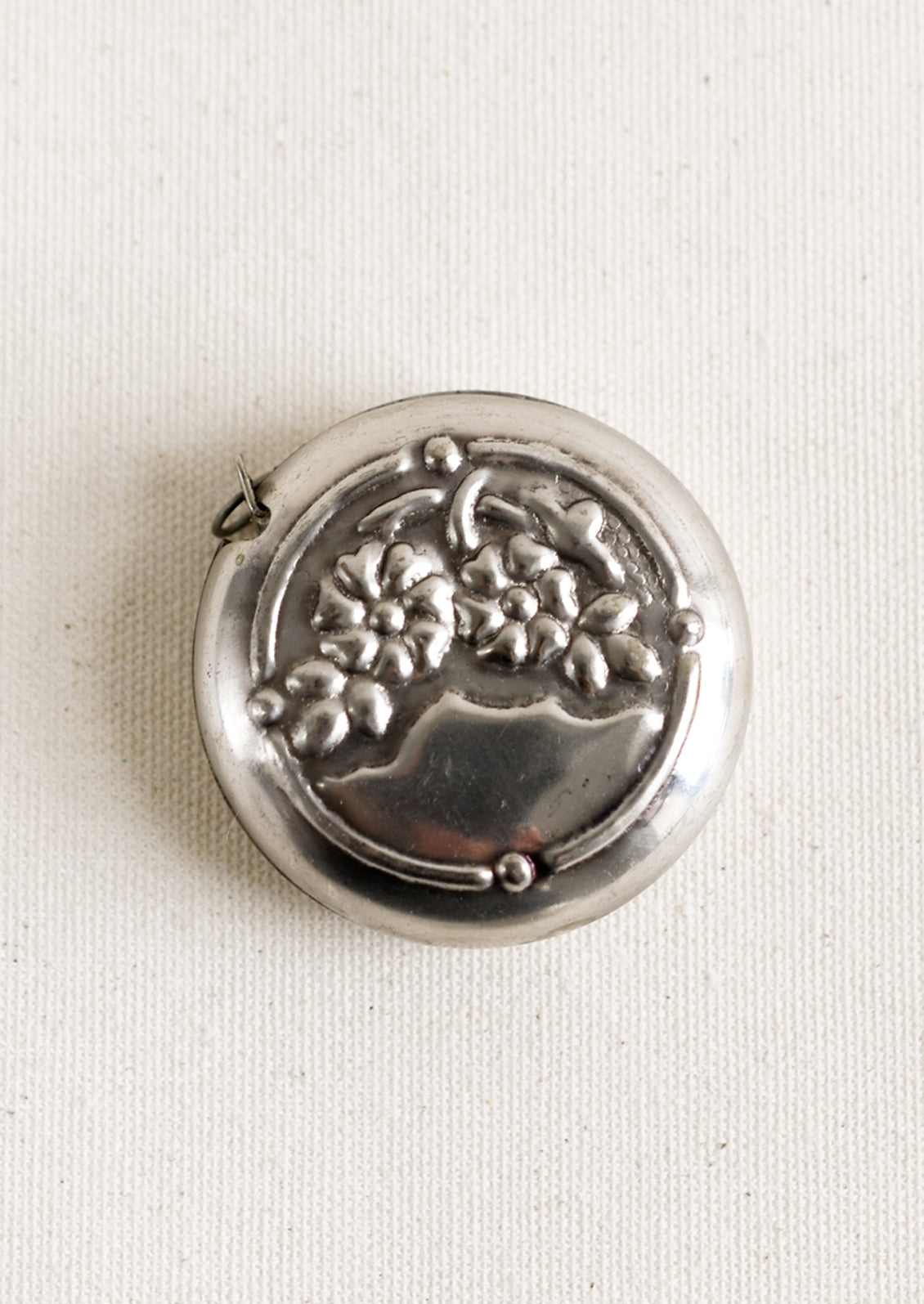 A round silver-tone measuring tape with embossed floral pattern.