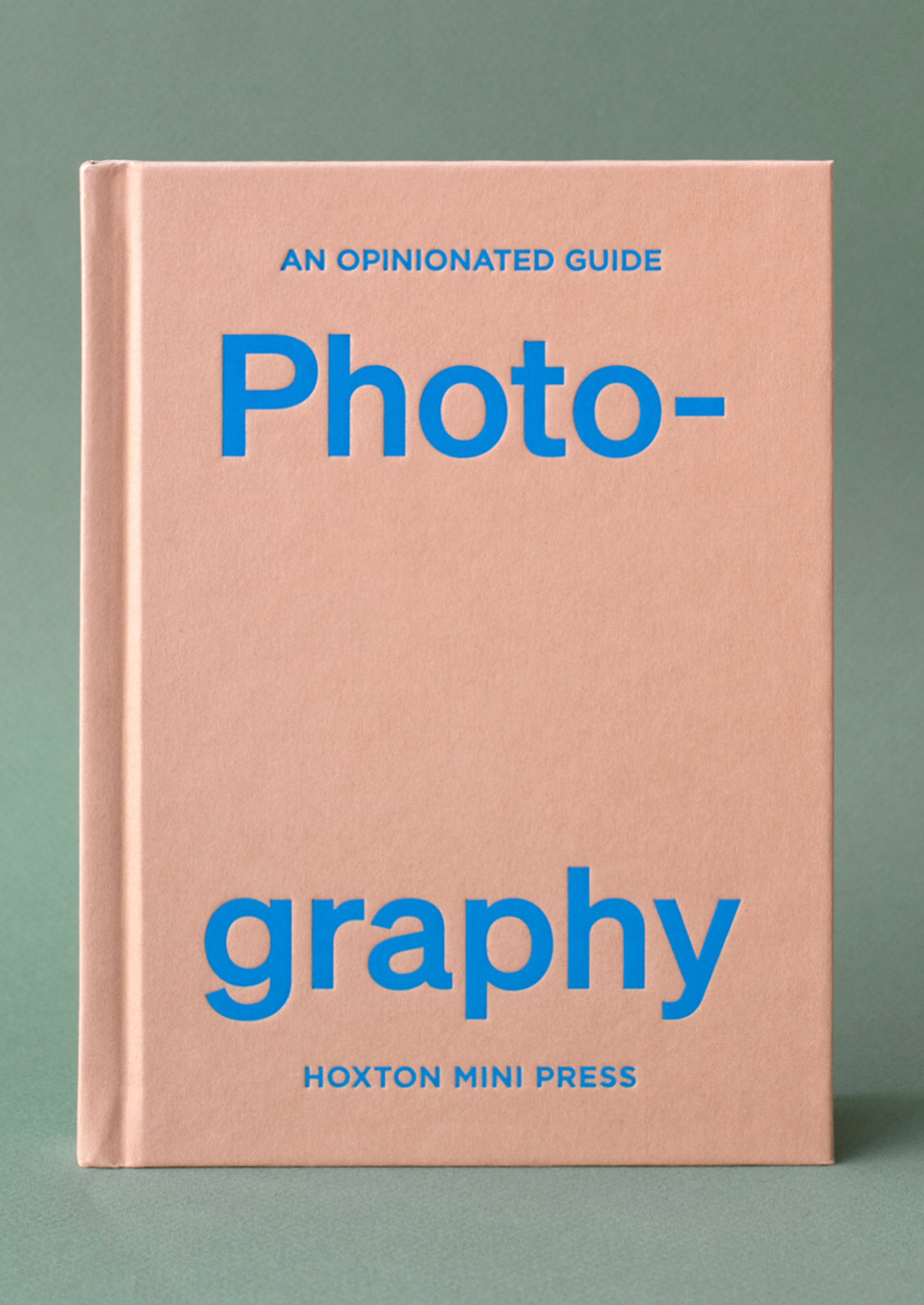 A pink hardcover book with blue lettering titled "An Opinionated Guide To Photography".