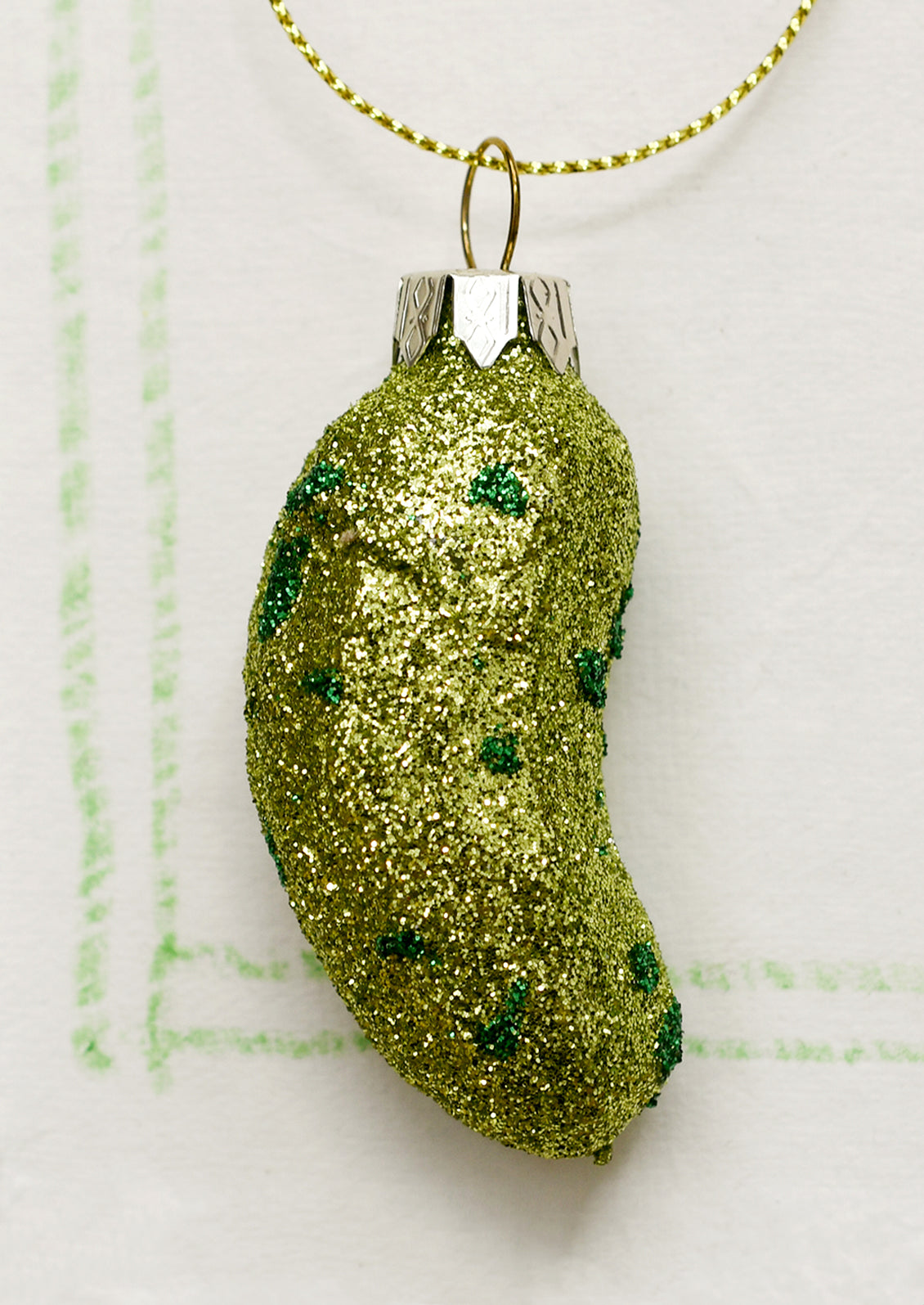 A small glass ornament of a pickle covered in green glitter.
