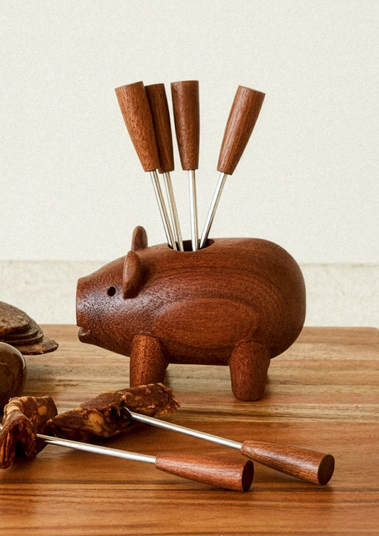 Wooden pig-shaped holder with metal skewers on a wooden surface