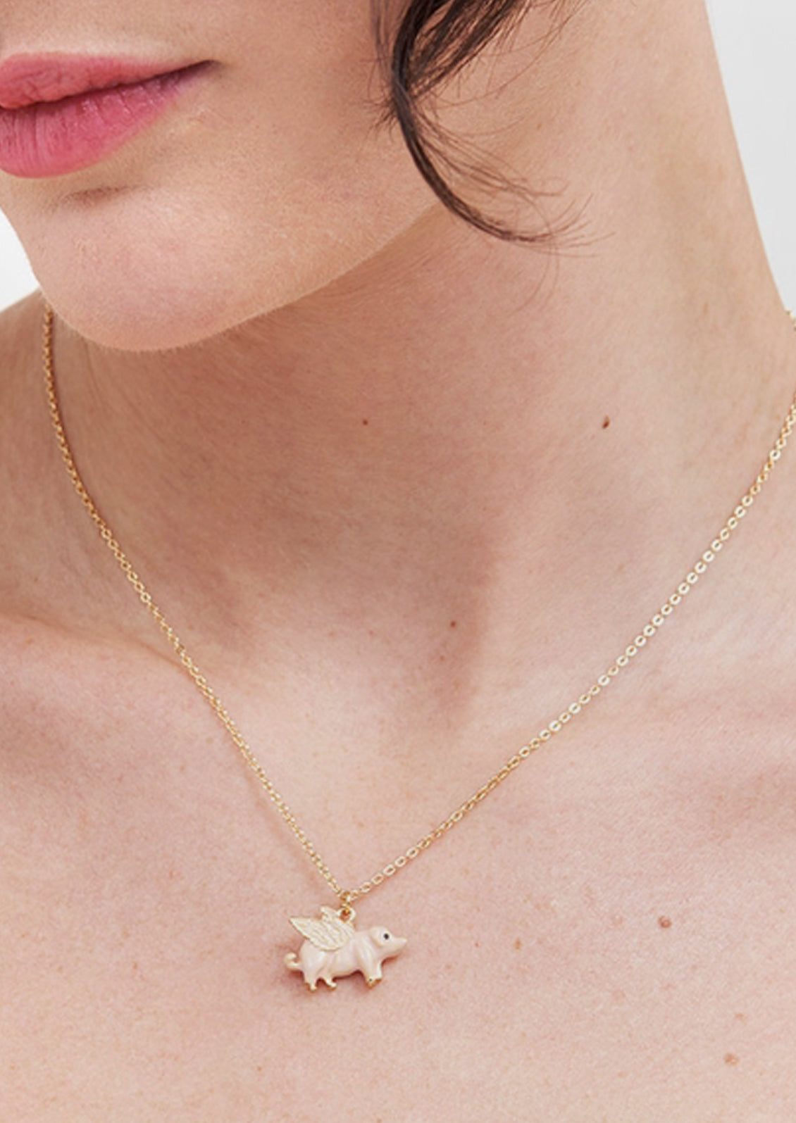 A gold plated chain necklace with a flying pig charm.